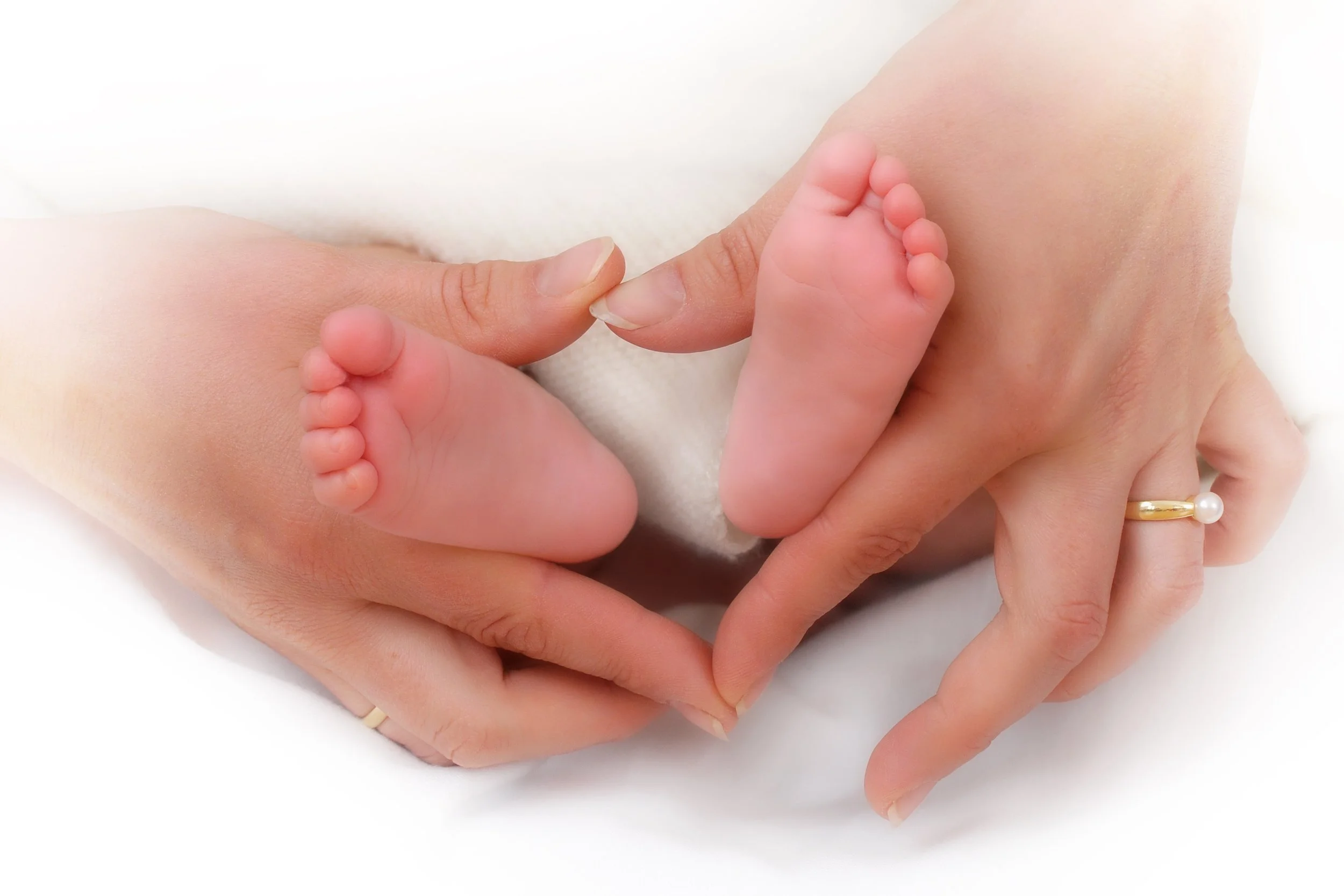 Kinderwillkommensfest: Nahaufnahme der Hände einer erwachsenen Person, die zarte Füße eines Babys halten, auf einem weißen Hintergrund, Hände formen ein Herz, Willkommen, geliebt