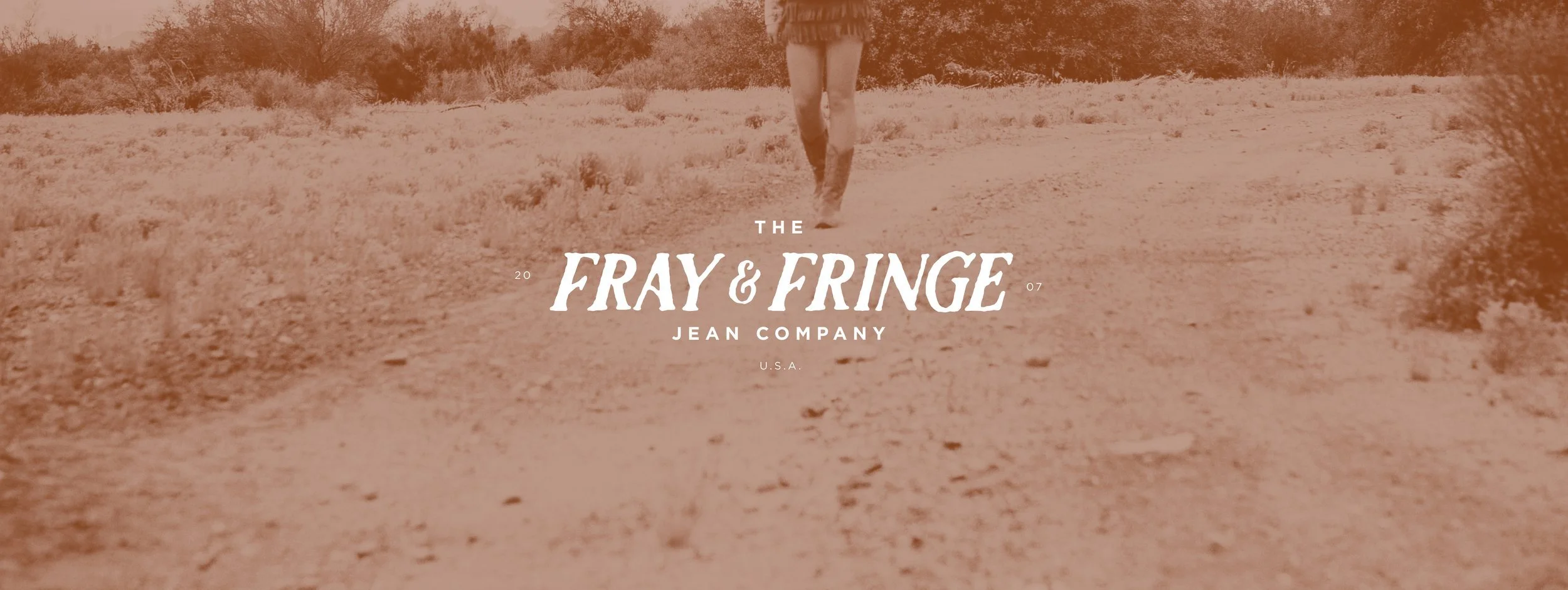 Image of a person walking on a dirt path in a desert landscape with bushes and trees in the background, overlaid with the text 'The Fray & Fringe Jean Company U.S.A. 2007'.