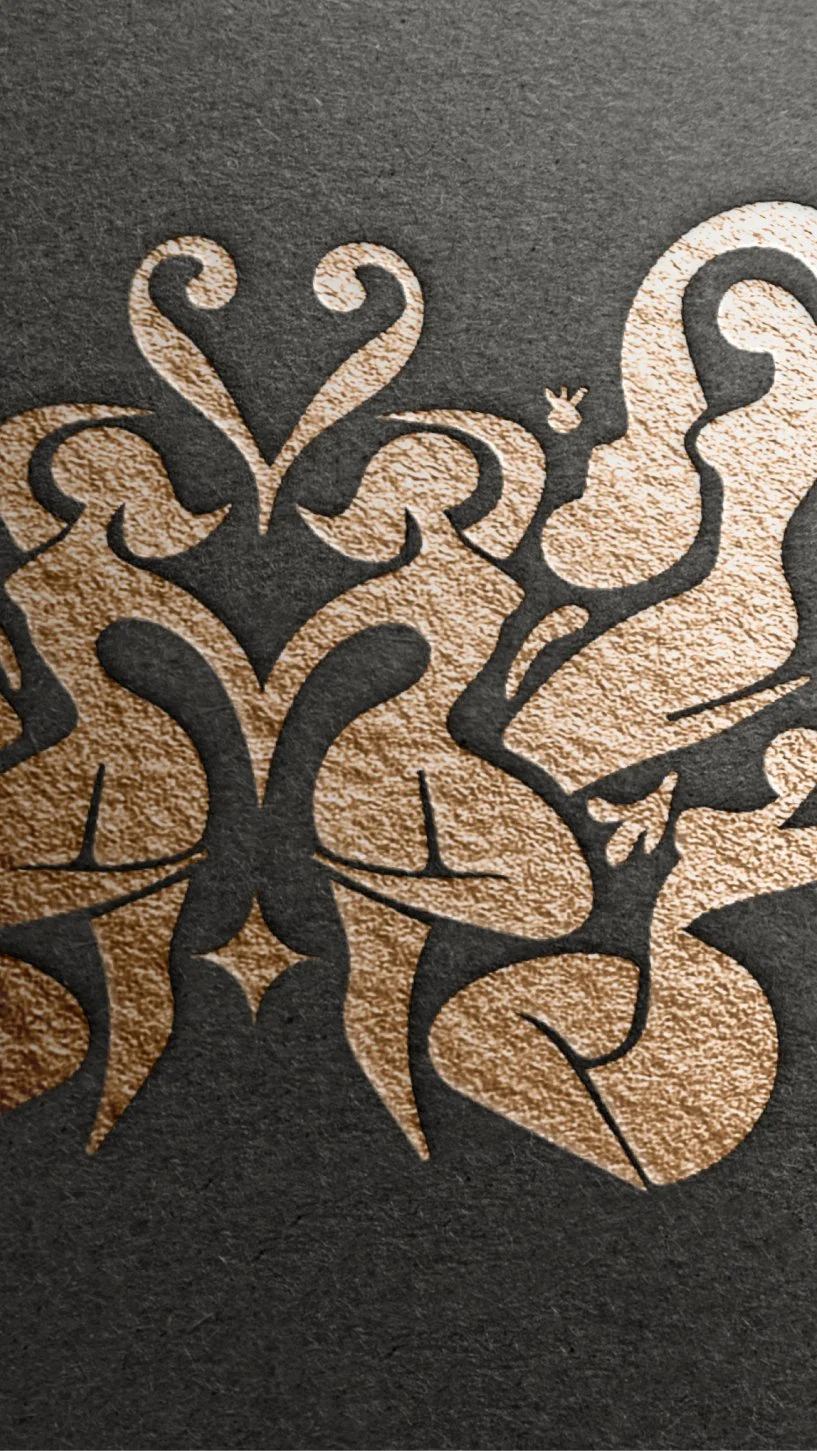 Close-up of a decorative black and gold design on textured paper, featuring ornate swirls and floral patterns.