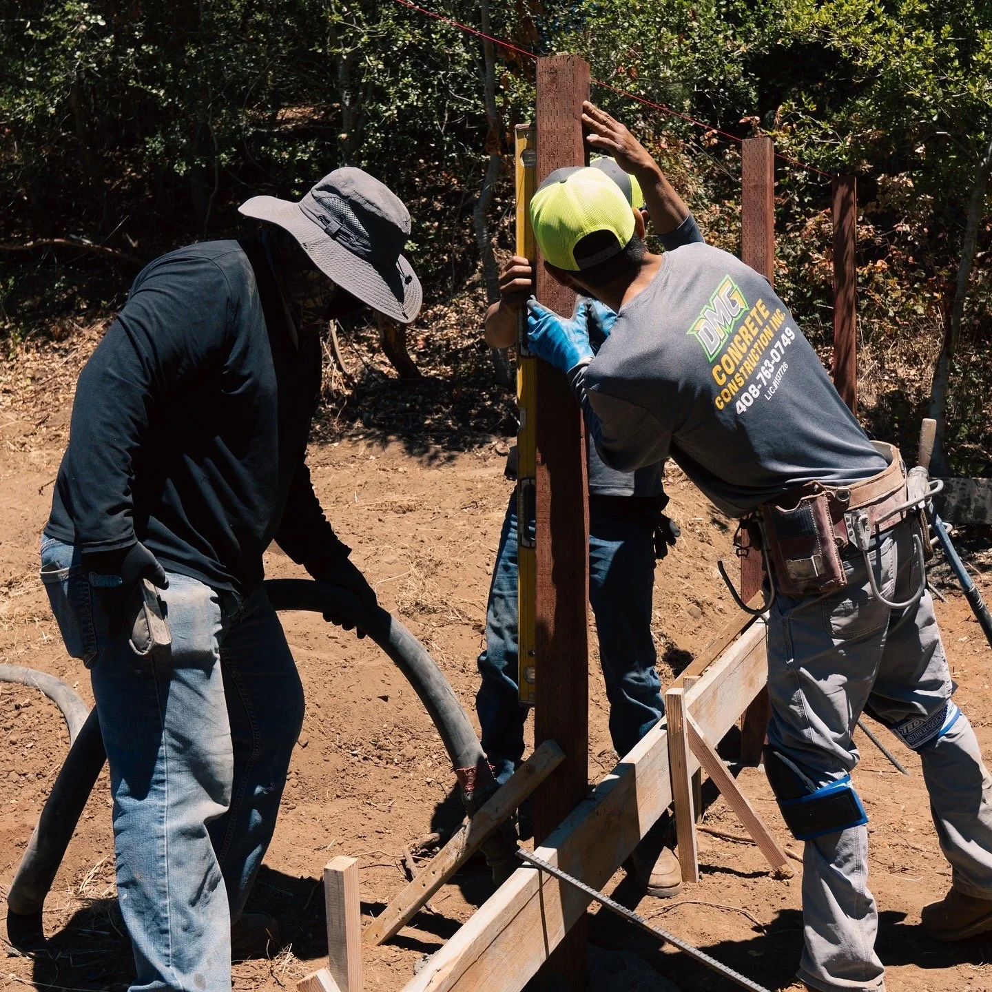 Three construction workers installing a wooden fence post outdoors during daytime.