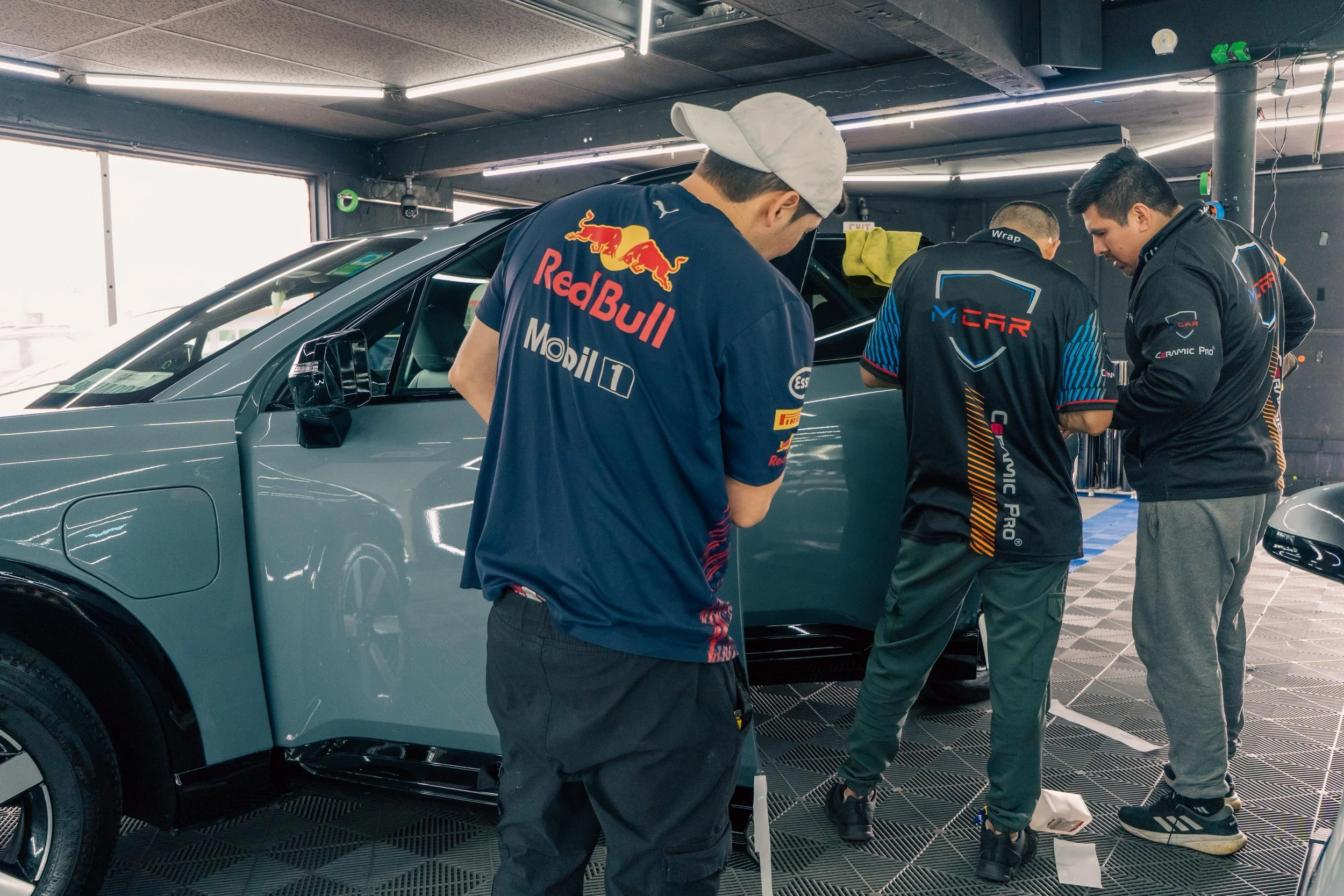 Three team members in Red Bull Racing gear inspecting a grey race car in a garage or workshop.