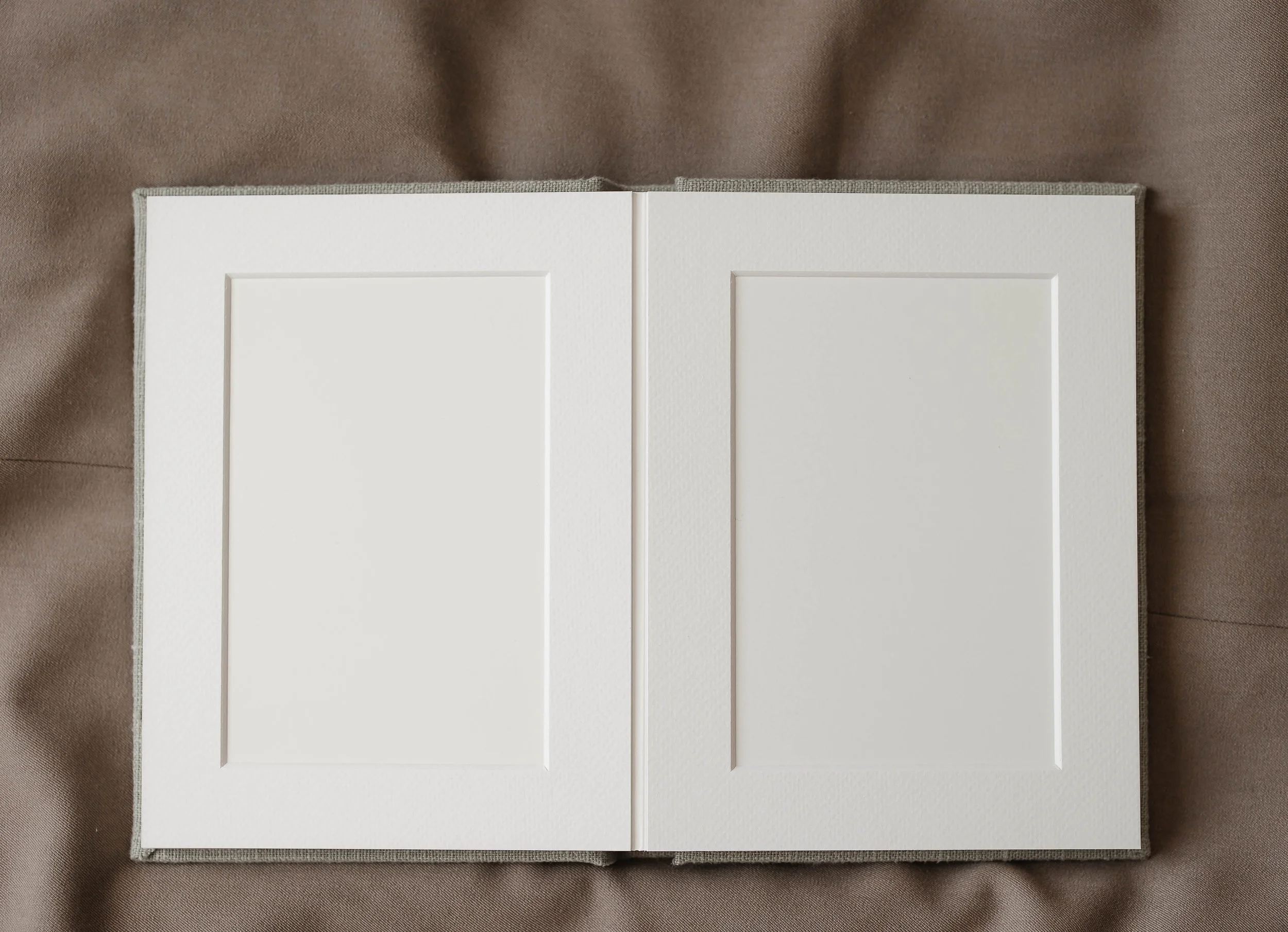 Åpen fotobok med hvite sider på en grå dukkeoverflate.