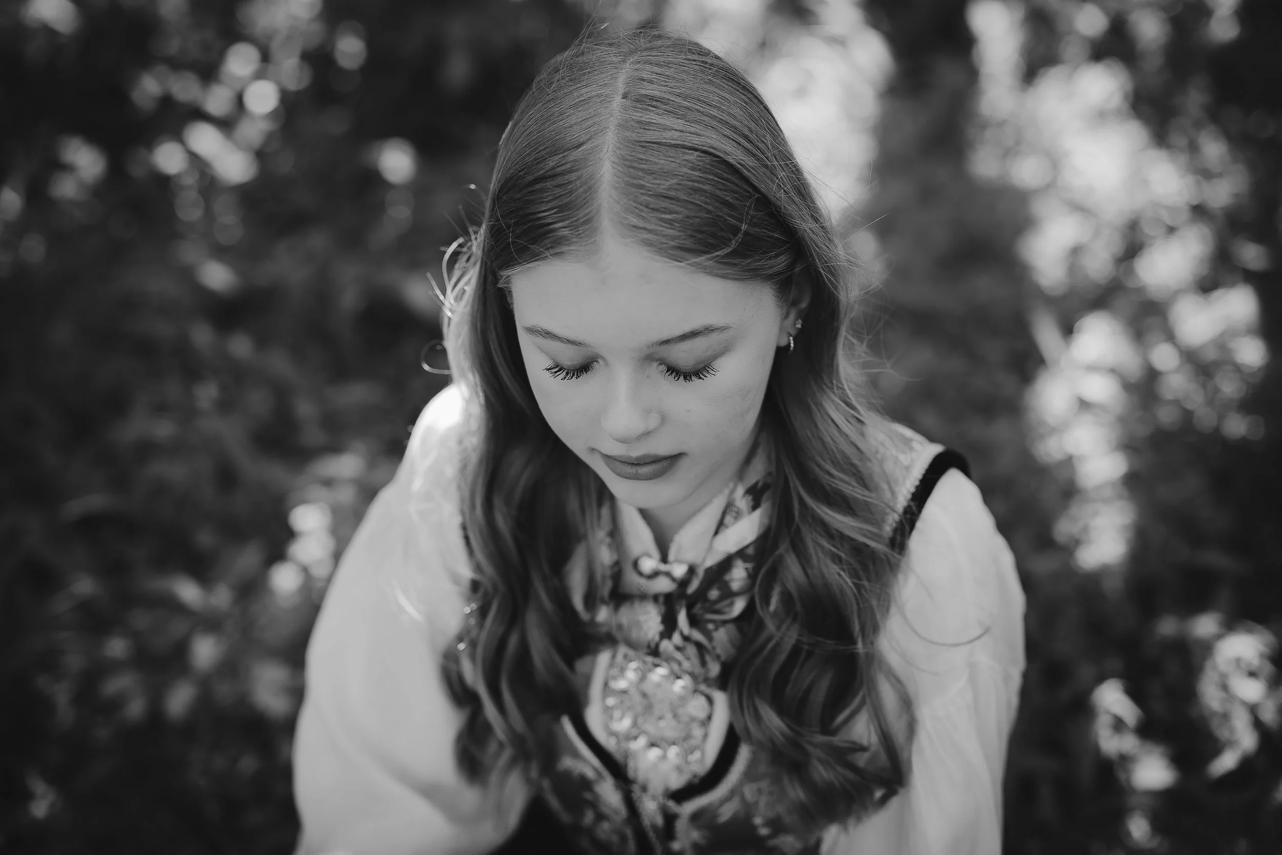 Et svart-hvitt bilde av en ung kvinne med lang, bølget hår, kledd i tradisjonell klær, sett nedenfra med lukket blikk i en utendørs setting.