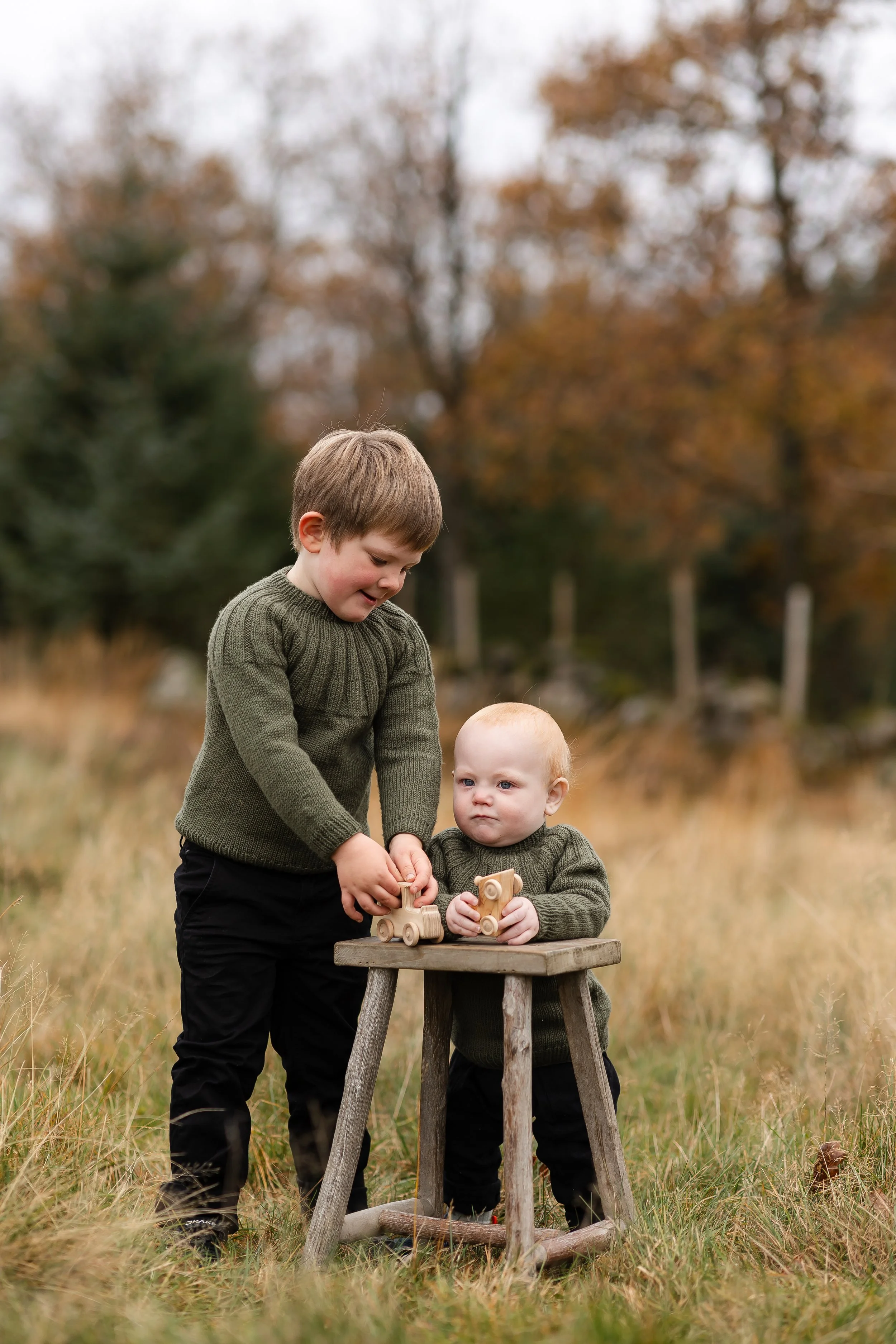 To barn leker med treleker i en utendørs setting med høstfarger og trær i bakgrunnen.