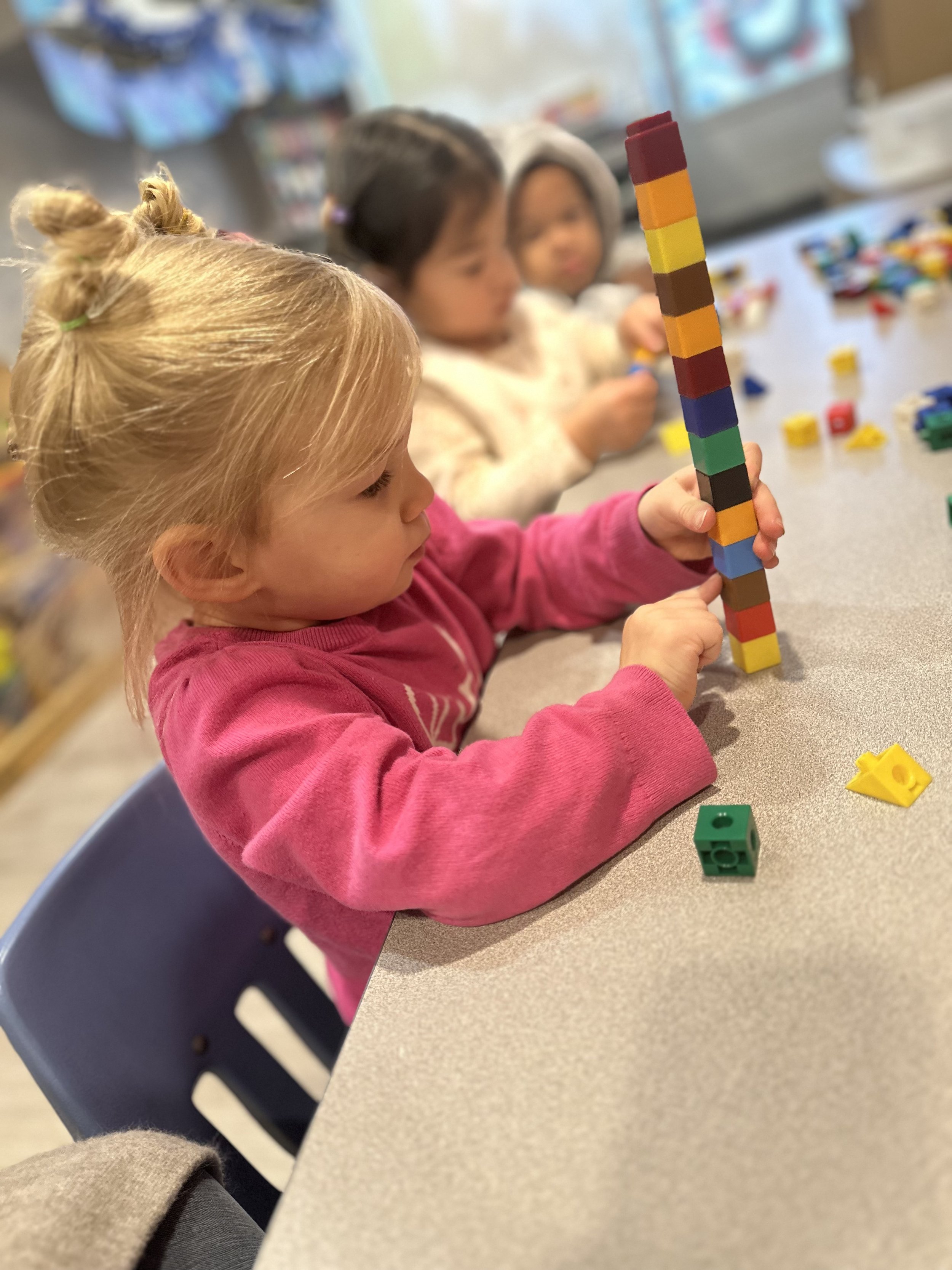 Children playing with colorful building blocks at a table in a classroom.