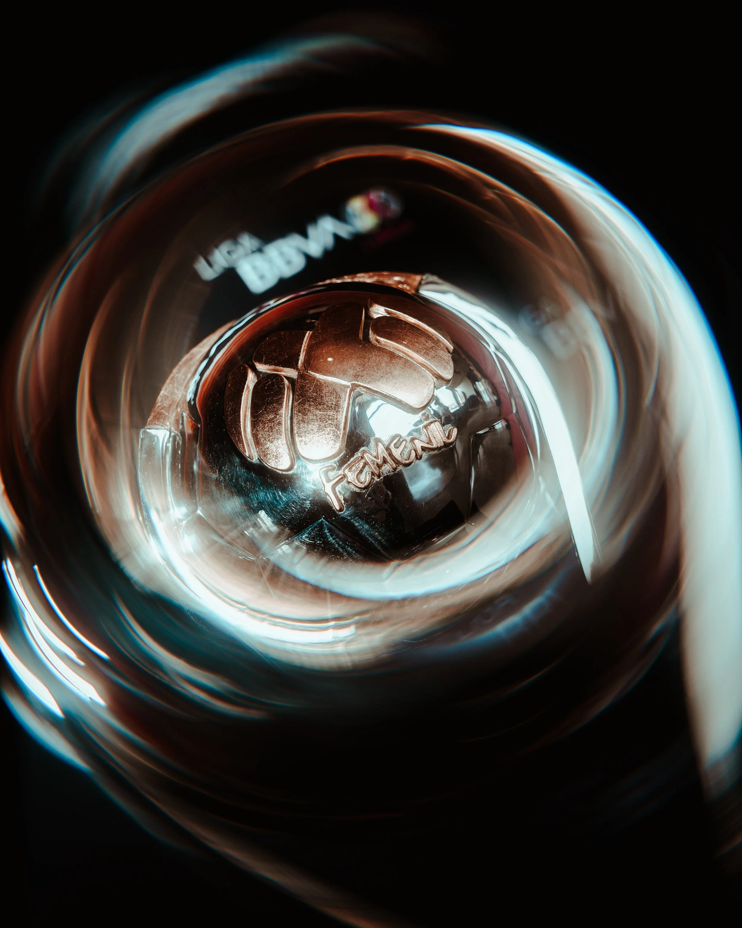 Close-up of a glass with a metal cap, seen from above, with the word 'FEMALE' inscribed on the cap, through the transparent surface and reflections.