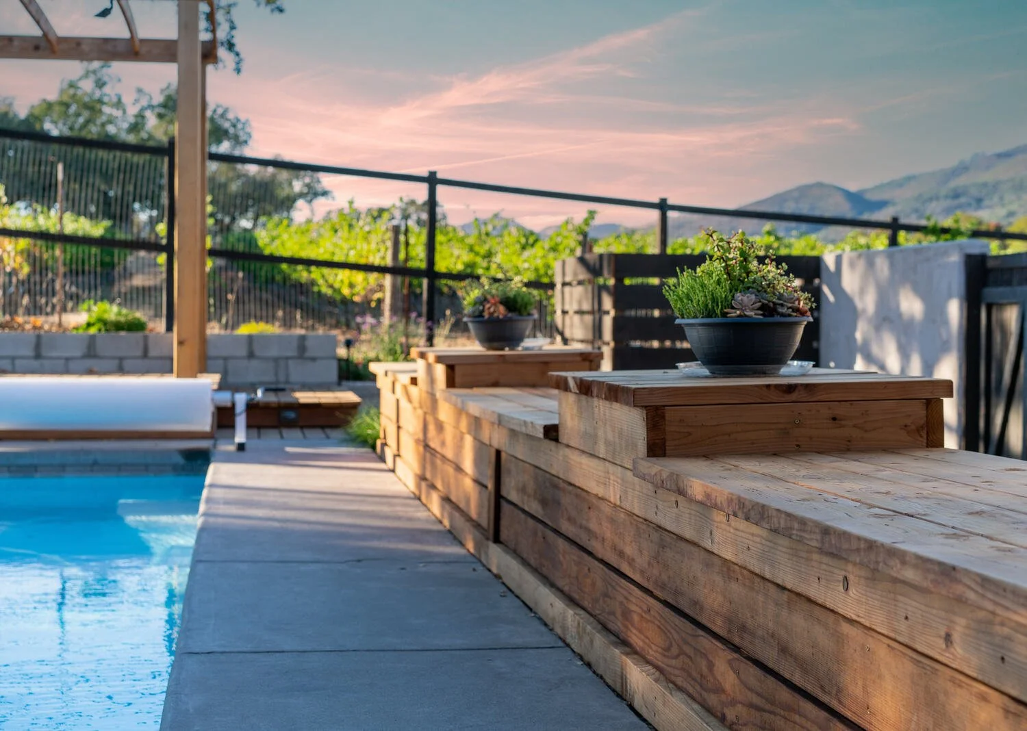 Raised wood deck with built-in planters beside a pool and vineyard view — BayTerra Landscapes