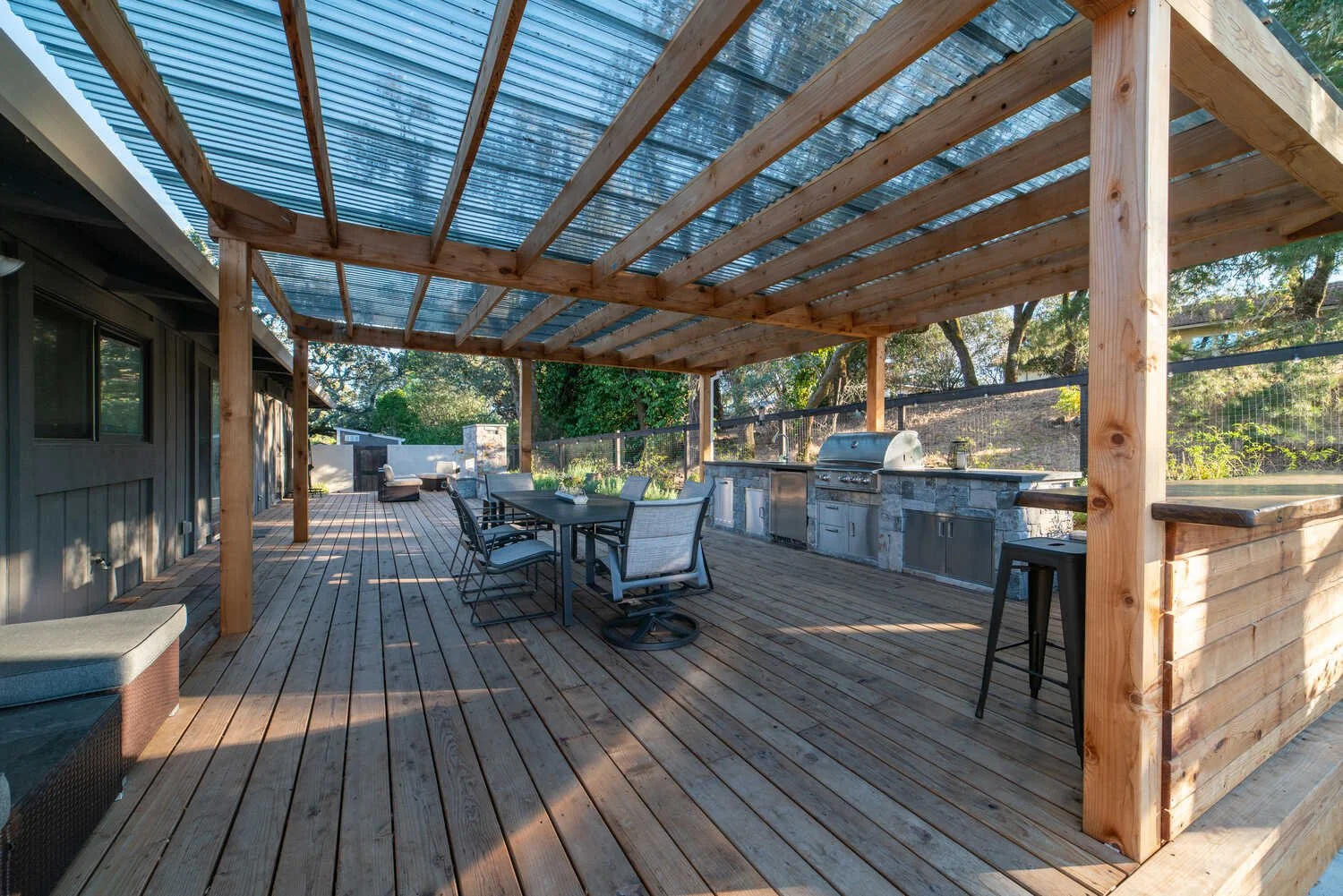 Covered wood deck with a dining set and outdoor kitchen under a timber pergola — BayTerra Landscapes