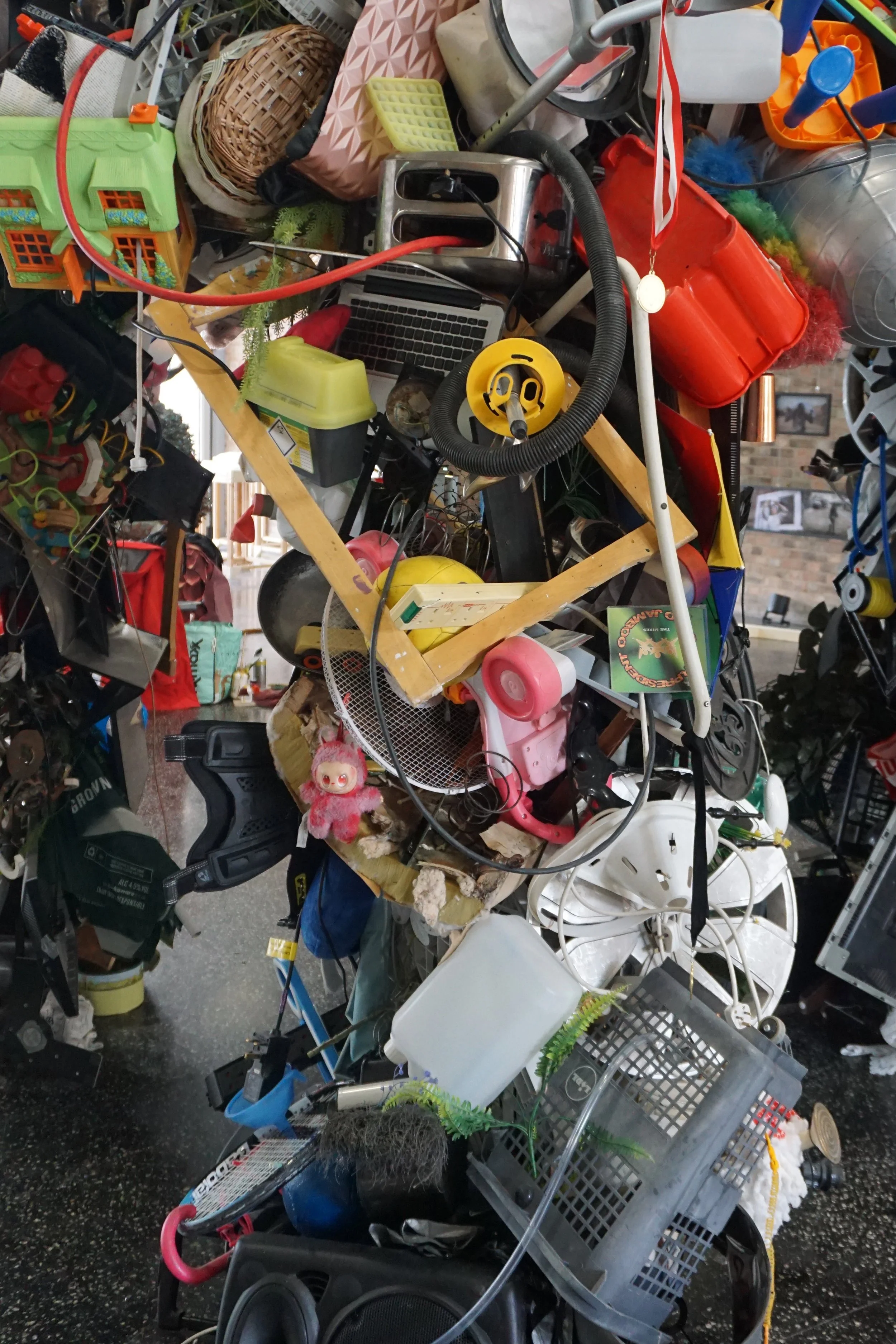 A large pile of miscellaneous household items and clutter, including toys, electronic devices, plastic containers, wires, and various small objects, stacked chaotically.
