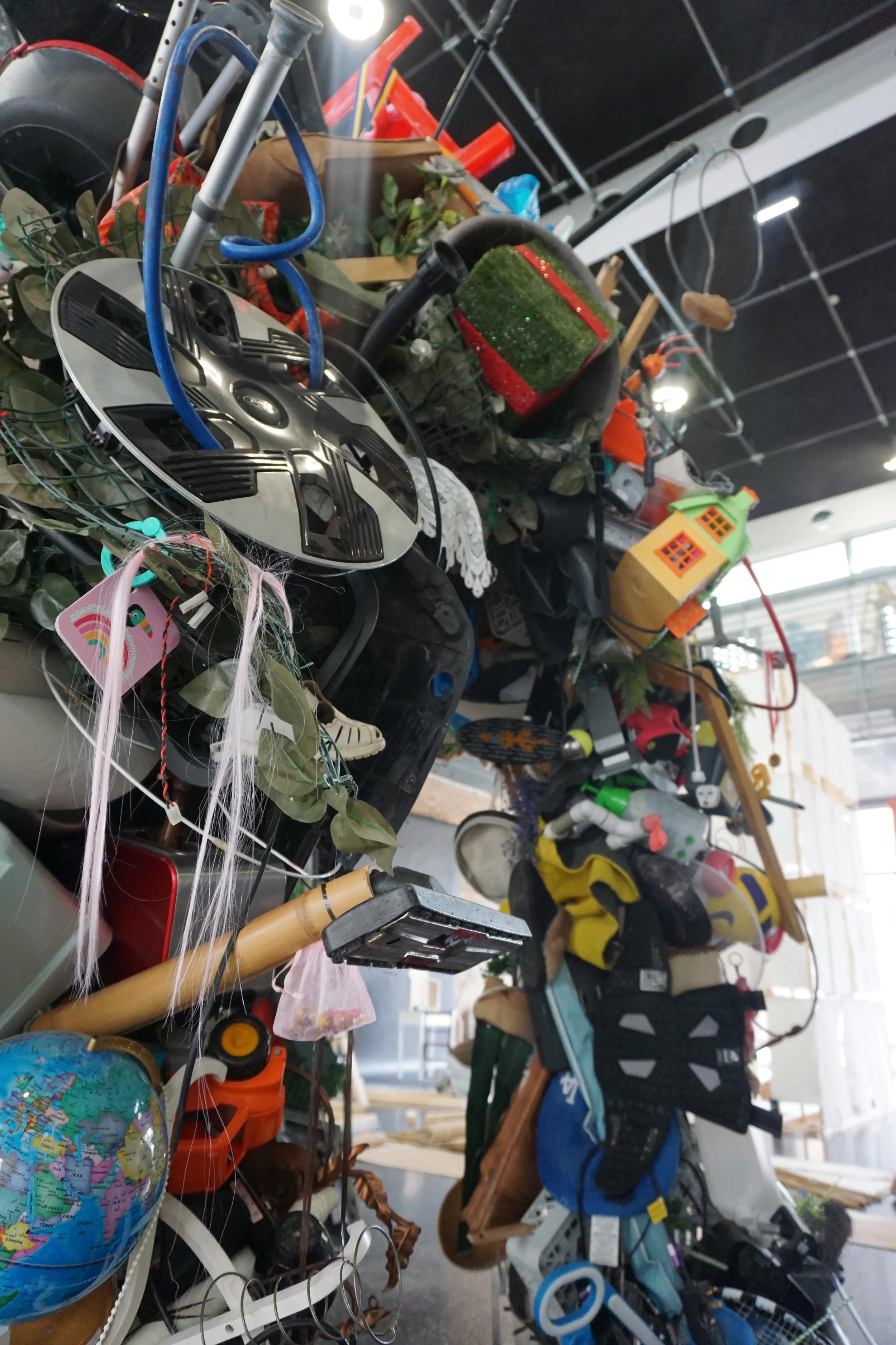 A cluttered assortment of various household items, toys, and tools on a table or shelf, including a globe, a helmet, a small house model, plants, and equipment.