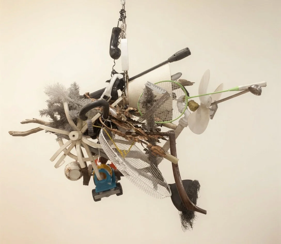 An art installation made from various household objects and natural materials suspended from the ceiling.