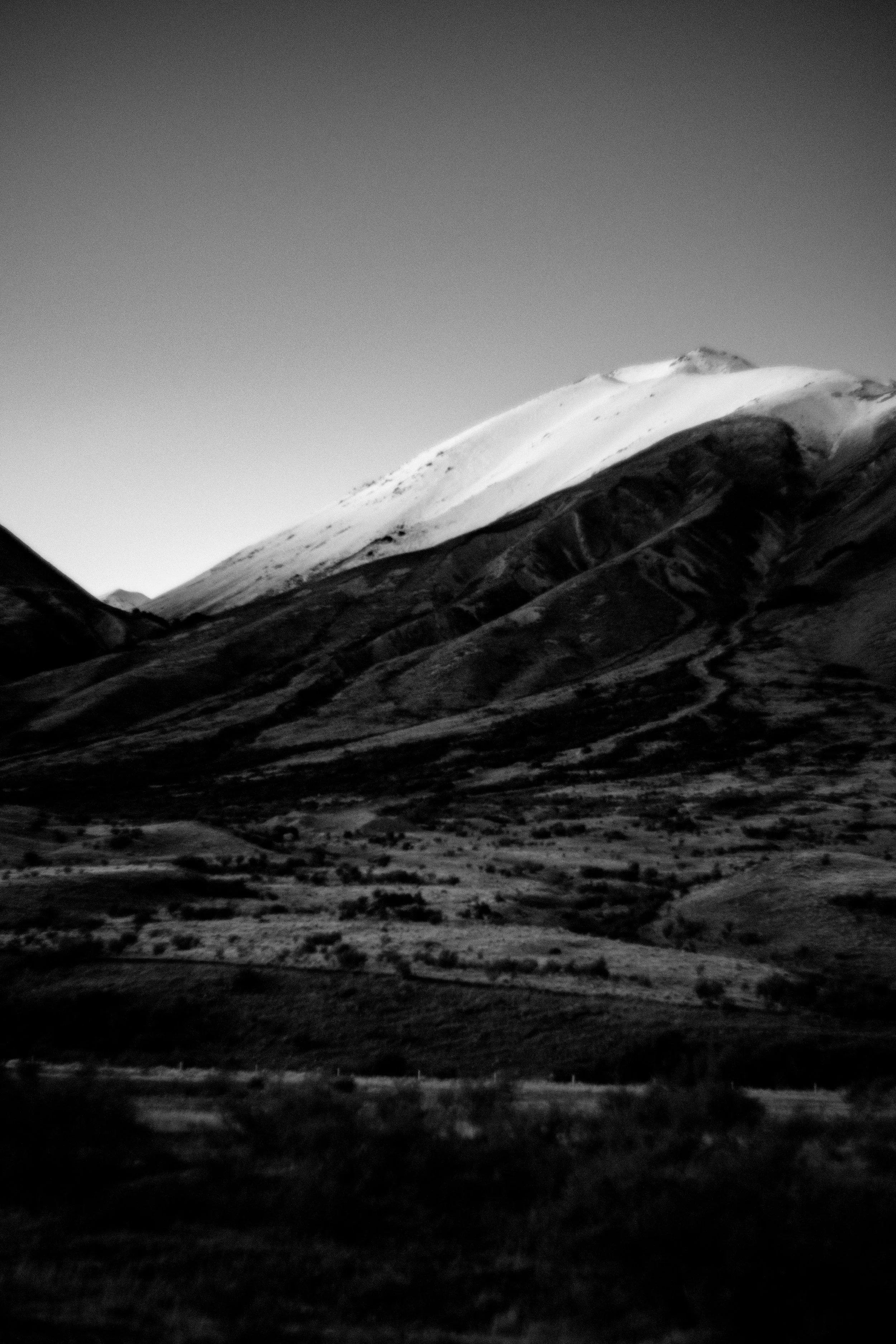 Black and white photo of a snow-capped mountain with a valley at the foreground.