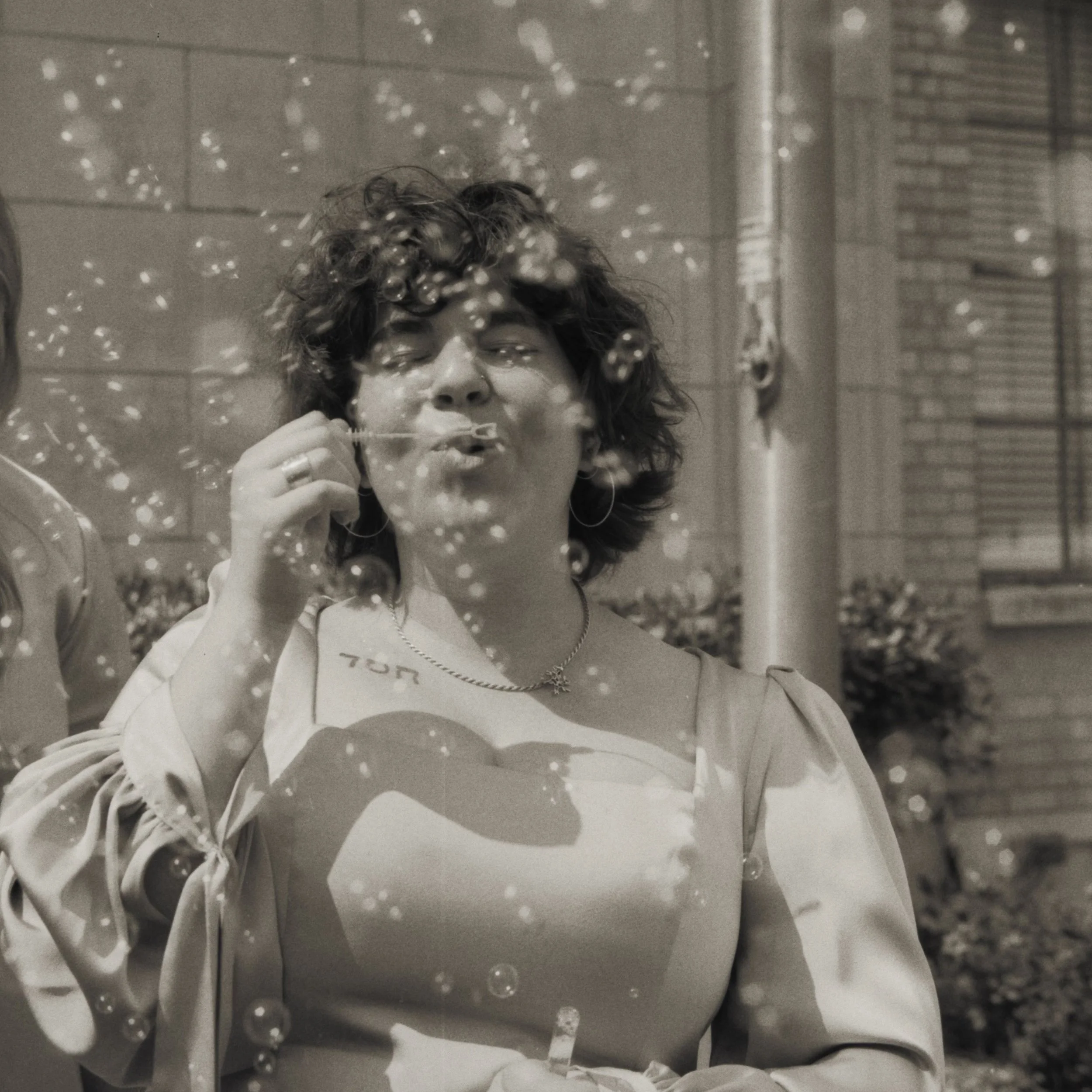 A woman with curly hair blowing bubbles from a bubble wand outdoors.