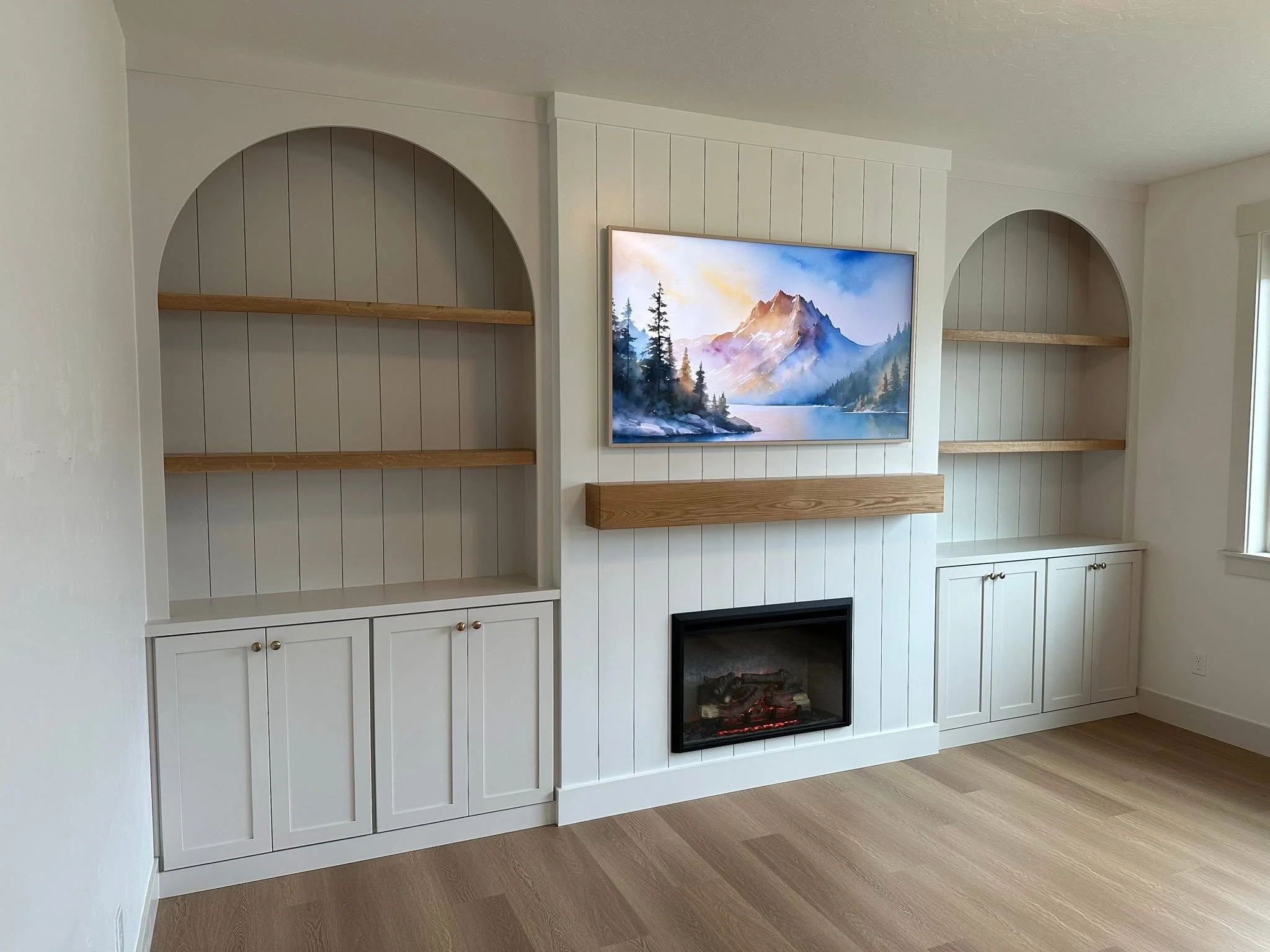 Custom arched built-in shelves with lower cabinets surrounding a shiplap fireplace and floating wood mantel in Meridian, Idaho.