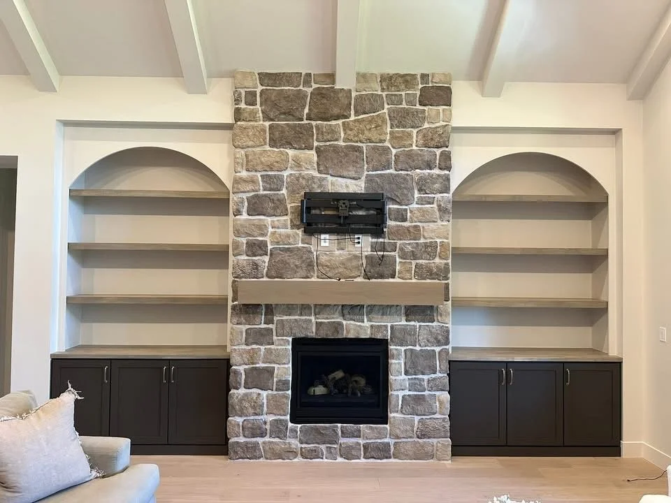 Custom arched built-in cabinets with open shelving surrounding a floor-to-ceiling stone fireplace in Kuna, Idaho.