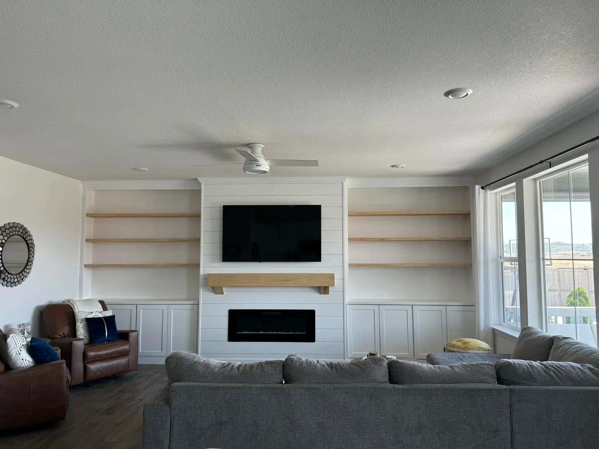 Custom living room built-ins featuring white cabinetry, floating oak shelves, and a shiplap fireplace surround in Caldwell, Idaho.