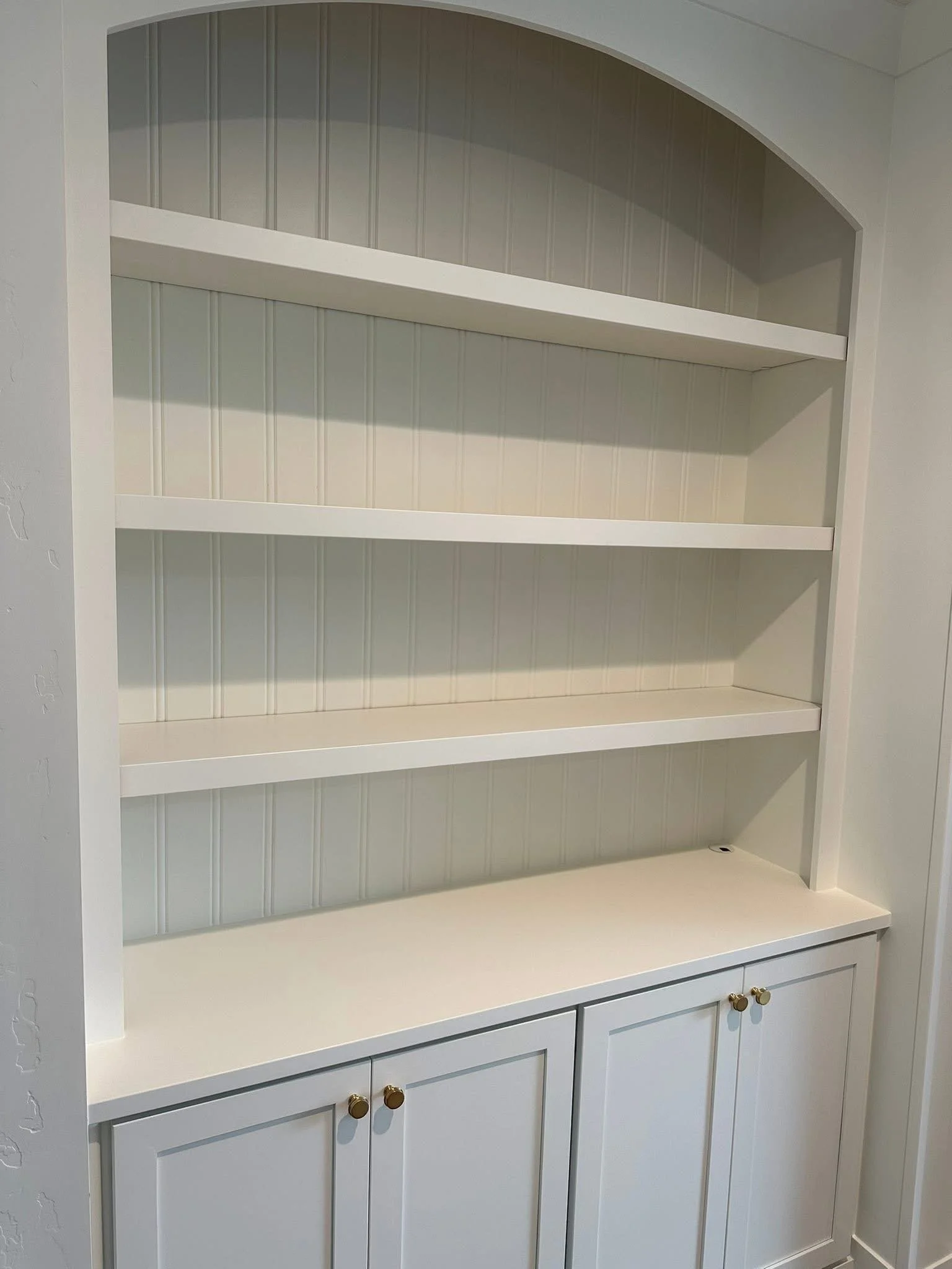 Close-up of a custom white arched built-in bookshelf with beadboard backing and lower storage cabinets in Star, Idaho.