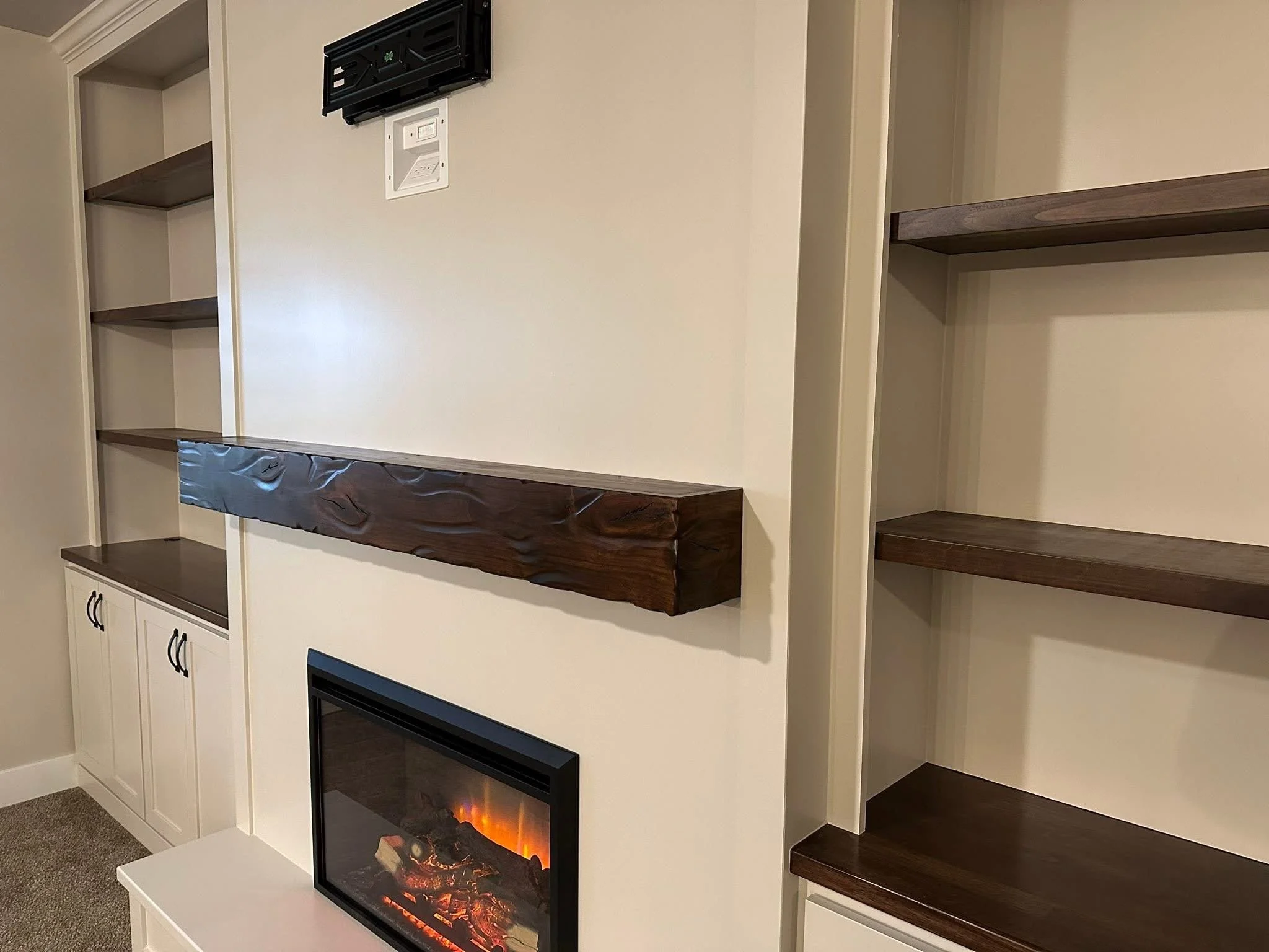 Close-up of a handcrafted floating wood mantel above an electric fireplace with custom built-in shelving in Meridian, Idaho.