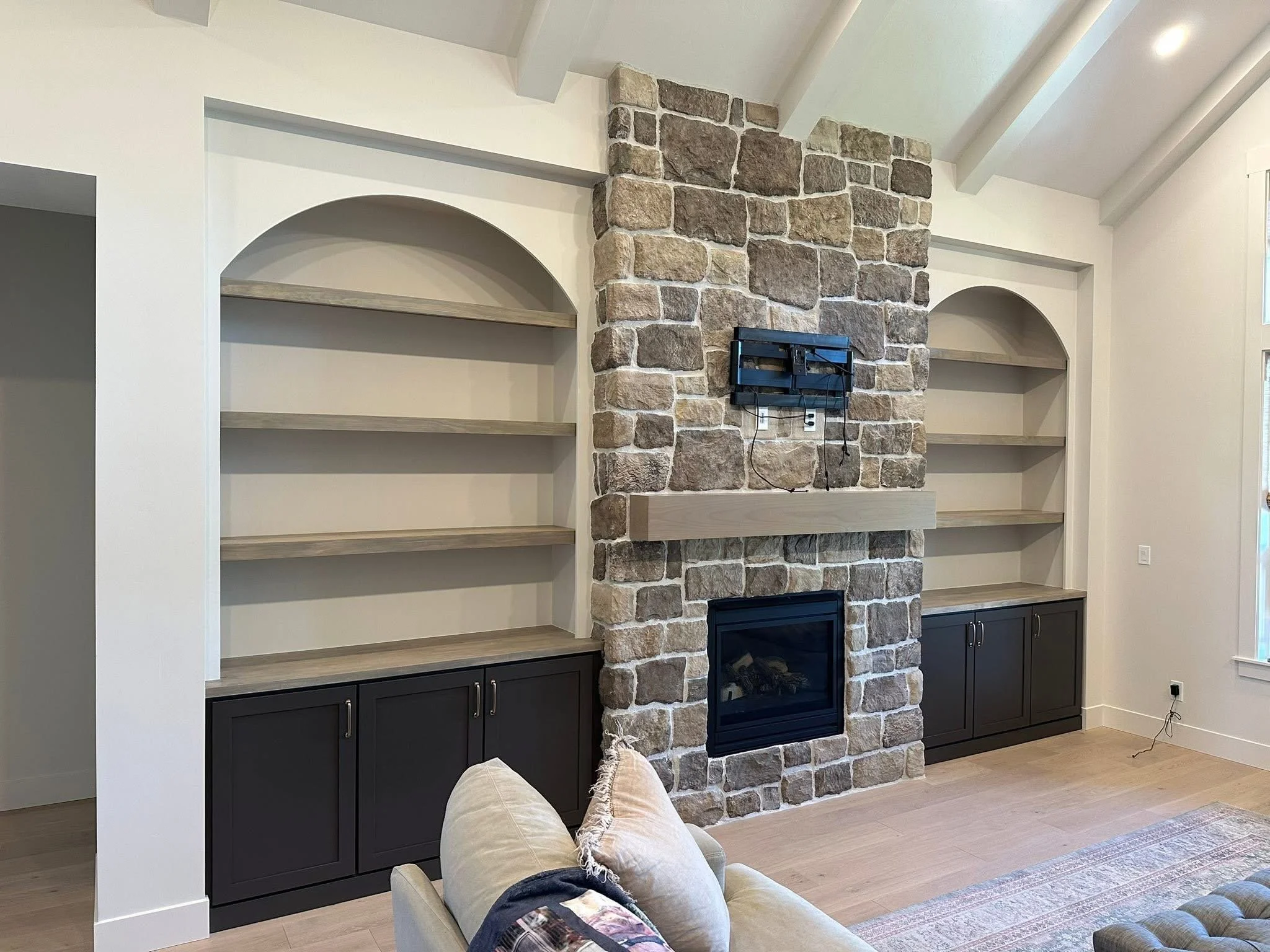 Custom entertainment center featuring arched built-in shelving, dark shaker cabinets, and a stone fireplace in Kuna, Idaho.