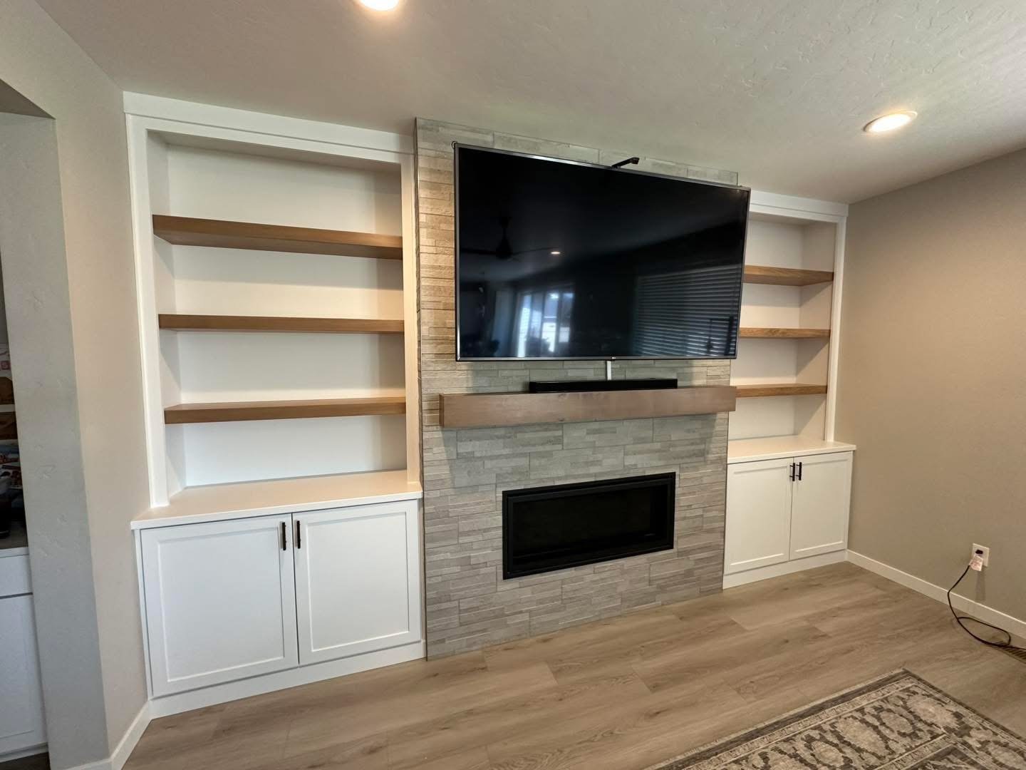 White shaker built-in cabinets with custom white oak floating shelves framing a modern fireplace in Meridian, Idaho.