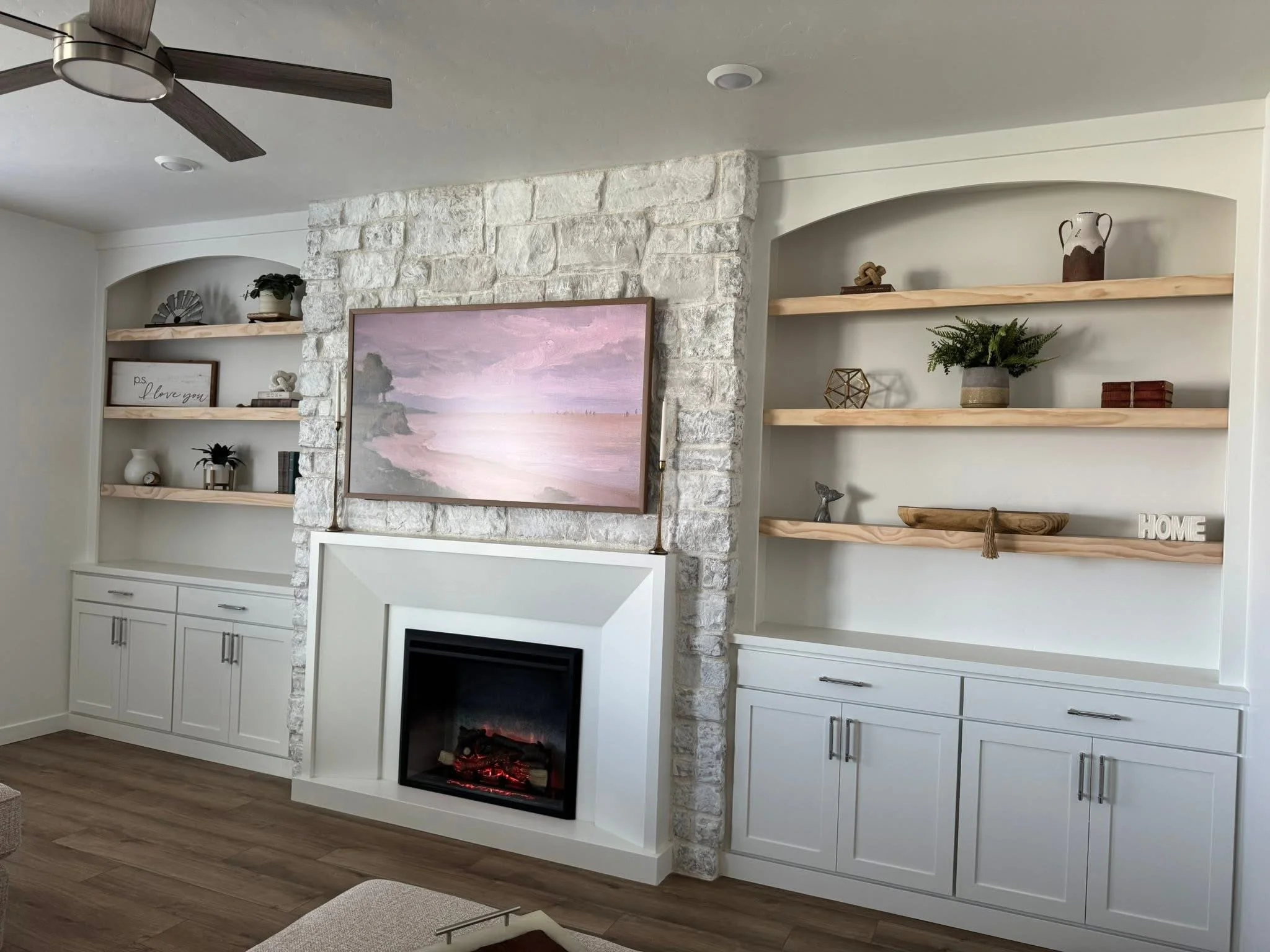 Custom entertainment center featuring a stone fireplace, arched shelving, floating wood shelves, and built-in cabinets in Caldwell, Idaho.