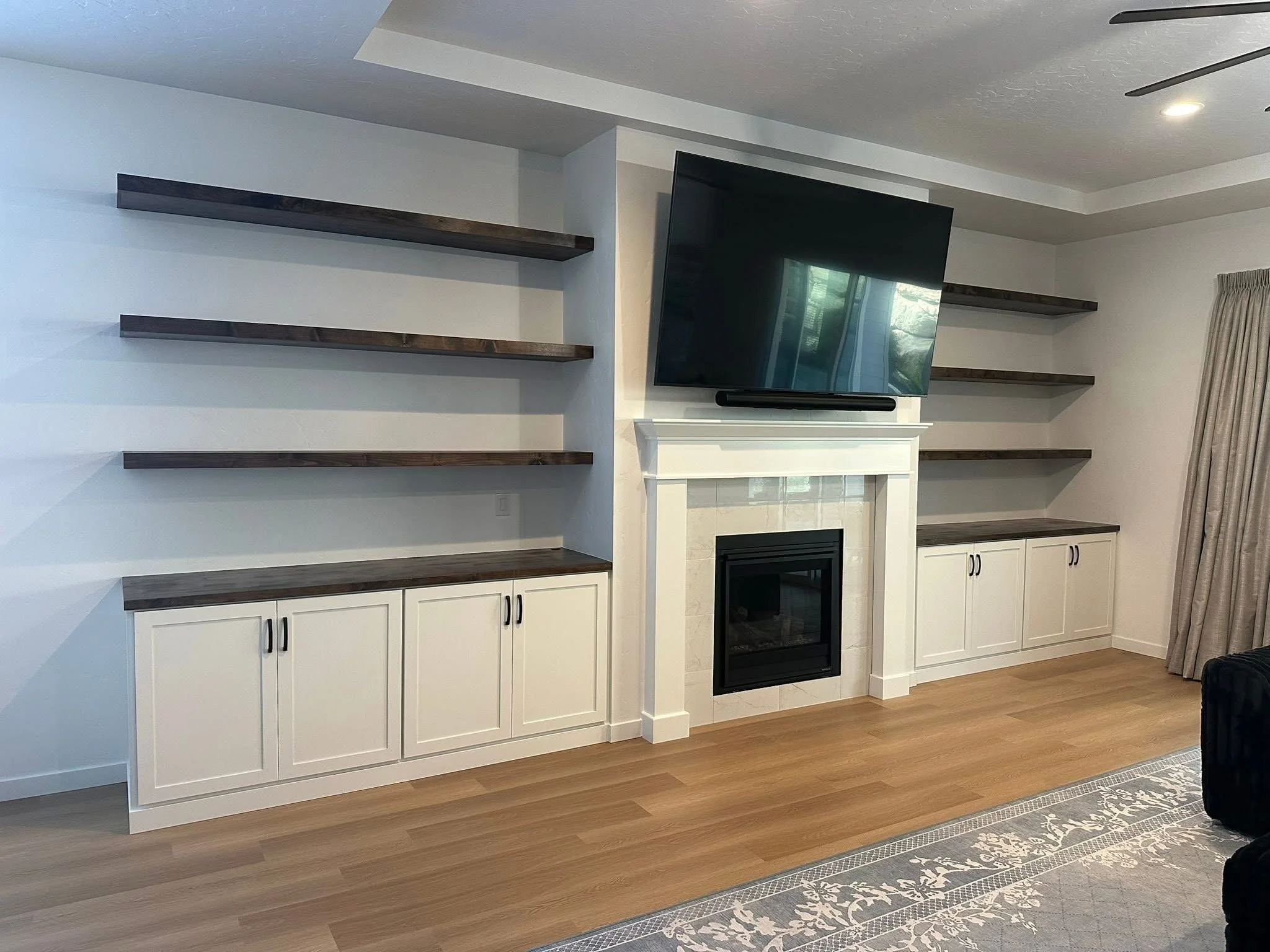 Custom entertainment wall featuring floating wood shelves, white built-in cabinets, and a fireplace in Star, Idaho.