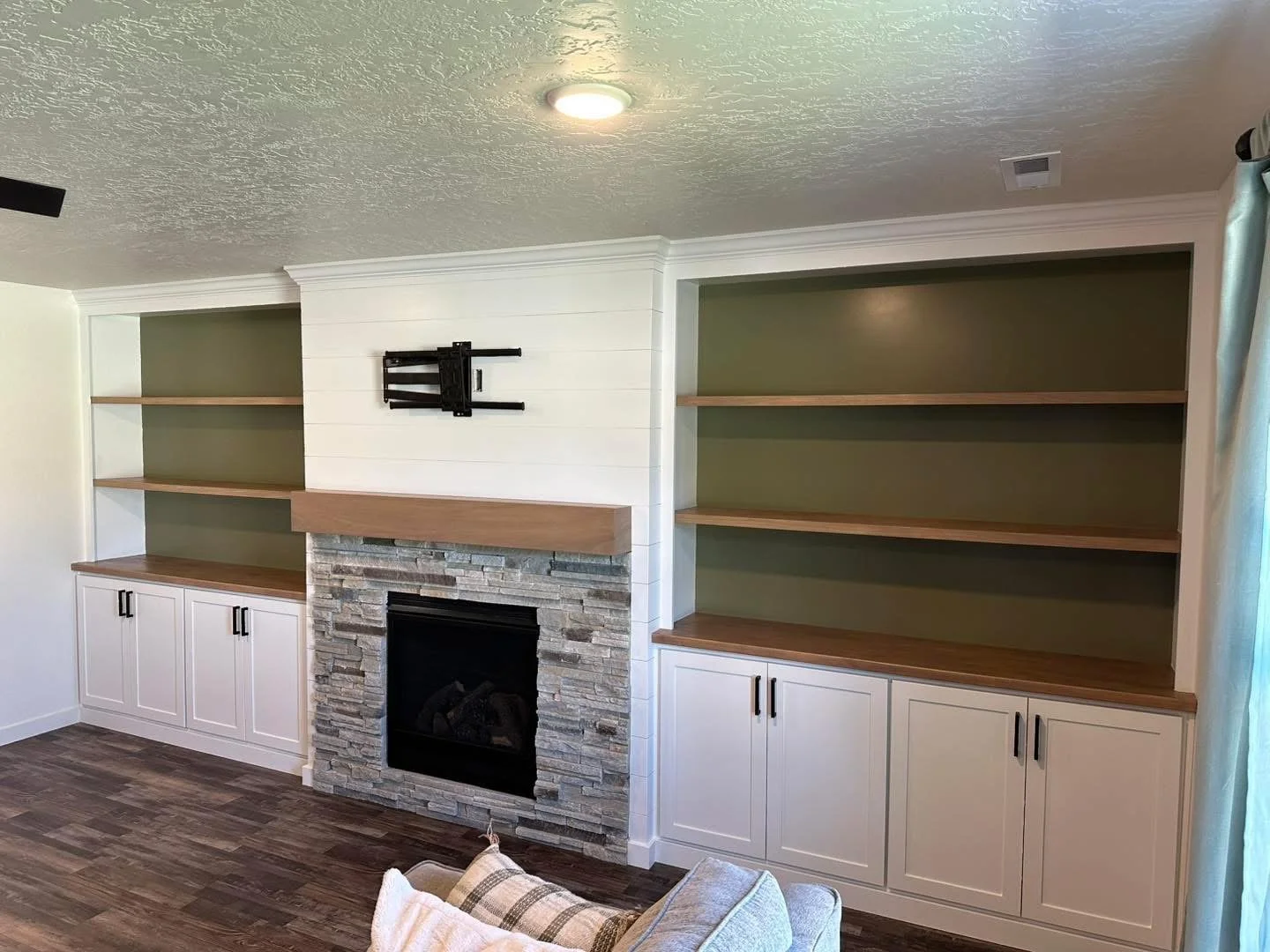 Custom white built-in cabinets with floating wood shelves around a stone fireplace.