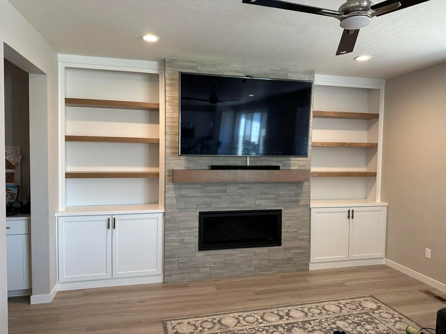 Custom living room built-in shelving surrounding a stone fireplace with white cabinetry and natural wood shelves in Meridian, Idaho.