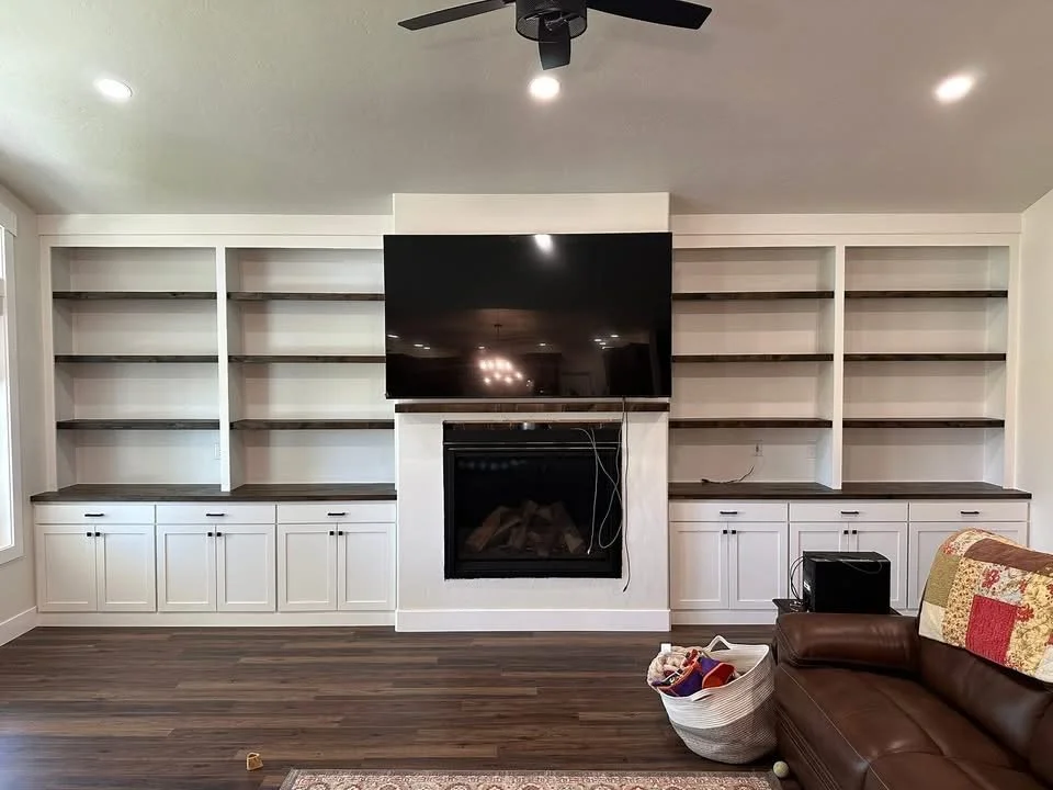 Wall-to-wall custom entertainment center with white shaker cabinets, dark wood floating shelves, and a fireplace in Wilder, Idaho.