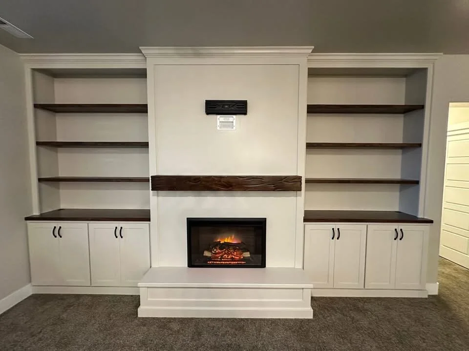 Custom built-in fireplace wall with white shaker cabinets, dark stained floating shelves, and a modern electric fireplace in Meridian, Idaho.