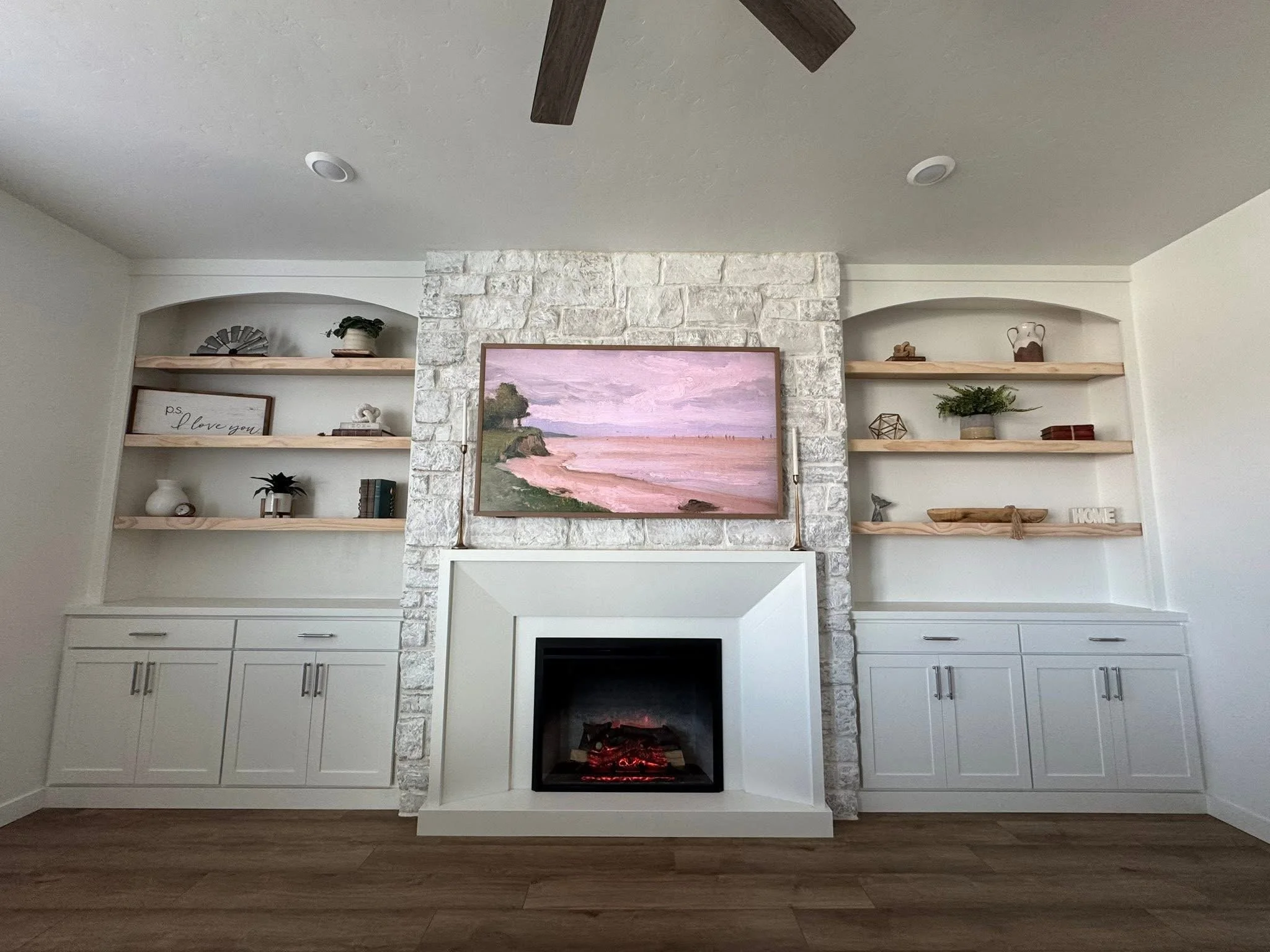 Custom stone fireplace with arched built-in shelves, floating wood shelves, and shaker cabinets in a Caldwell, Idaho living room.