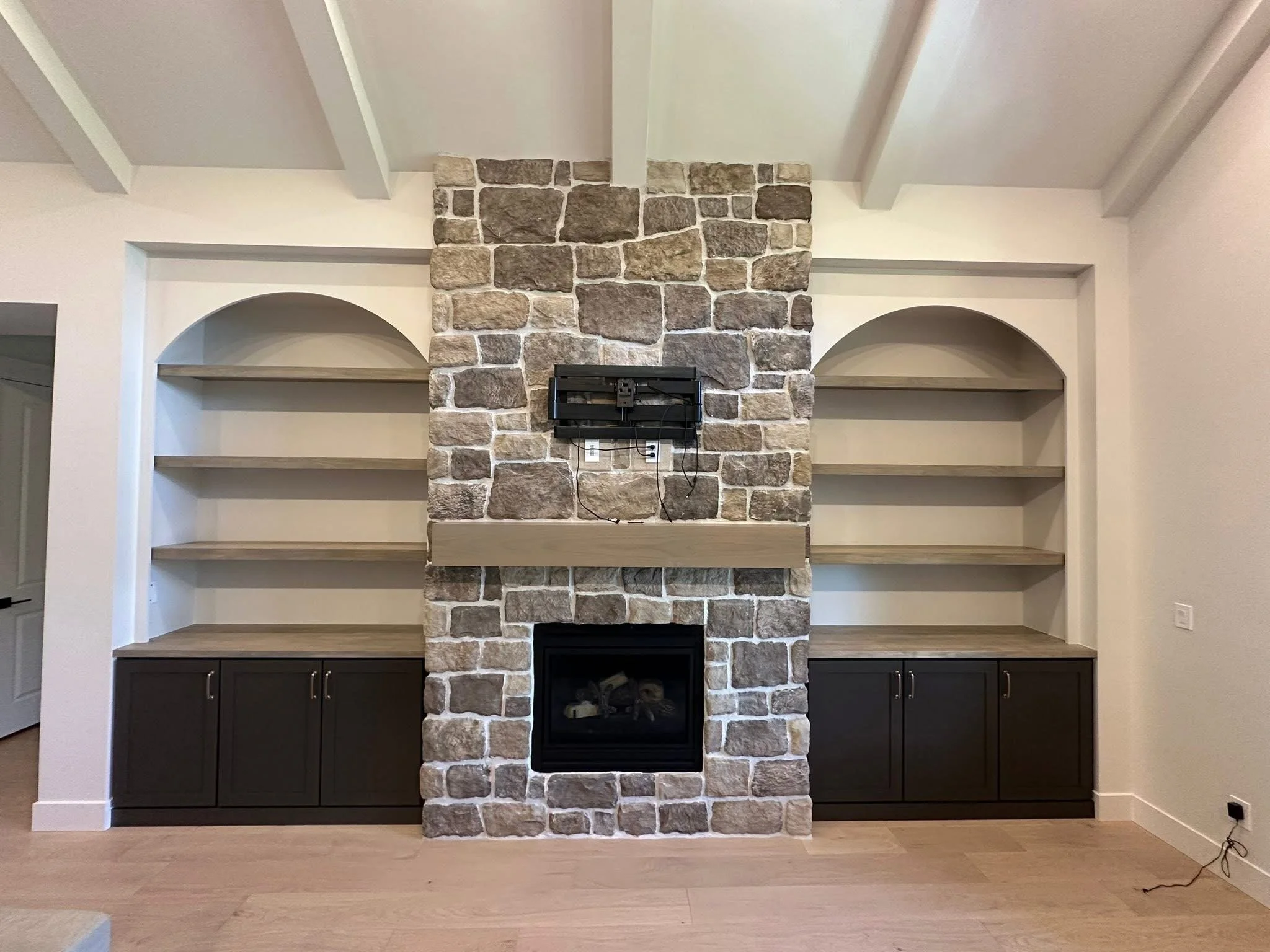 Custom living room built-ins with arched shelving, dark shaker cabinets, and a rustic stone fireplace in Kuna, Idaho.