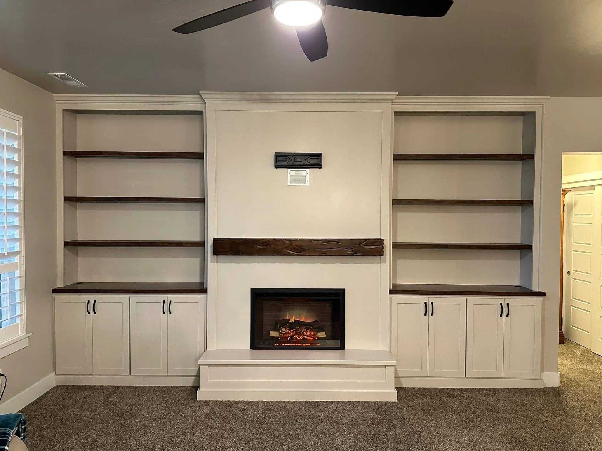Custom entertainment center with white built-in cabinets, floating wood shelves, and a modern electric fireplace in Meridian, Idaho.