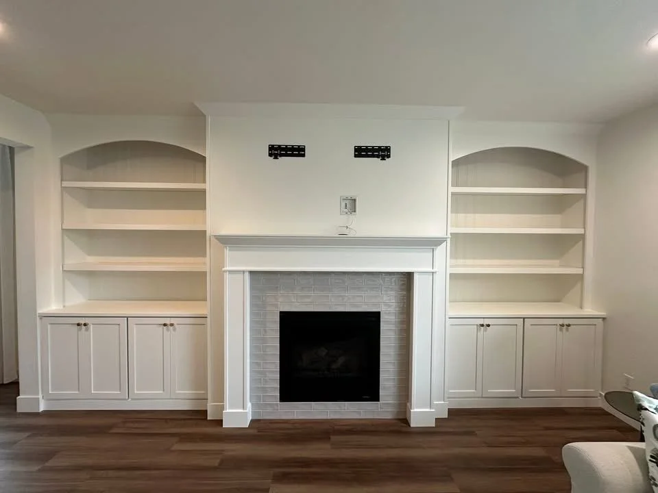 Custom arched built-in bookshelves with white shaker cabinets surrounding a fireplace in a Star, Idaho living room.