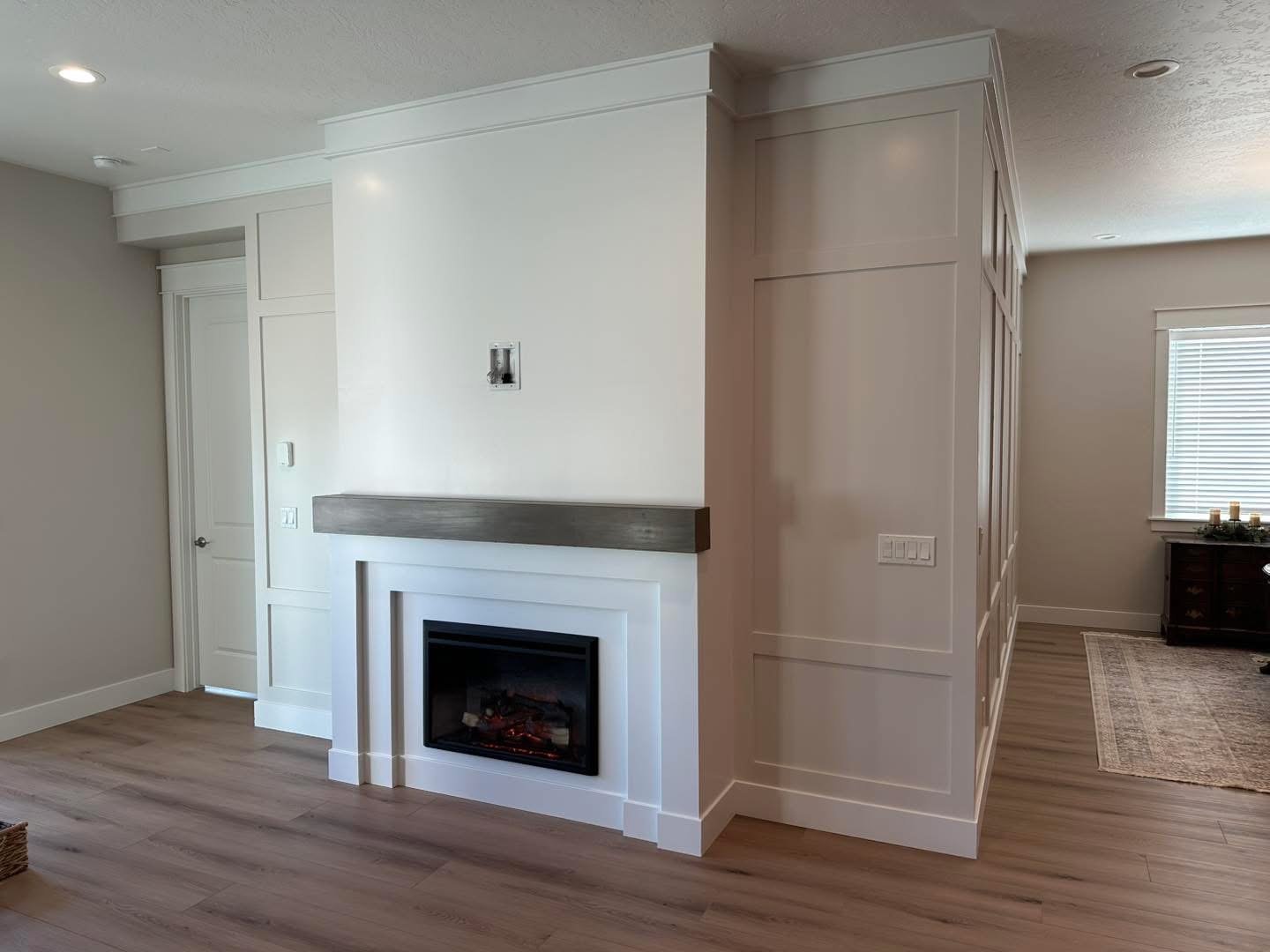 Angled view of a custom fireplace feature wall with a floating wood mantel and decorative wall trim in Meridian, Idaho.
