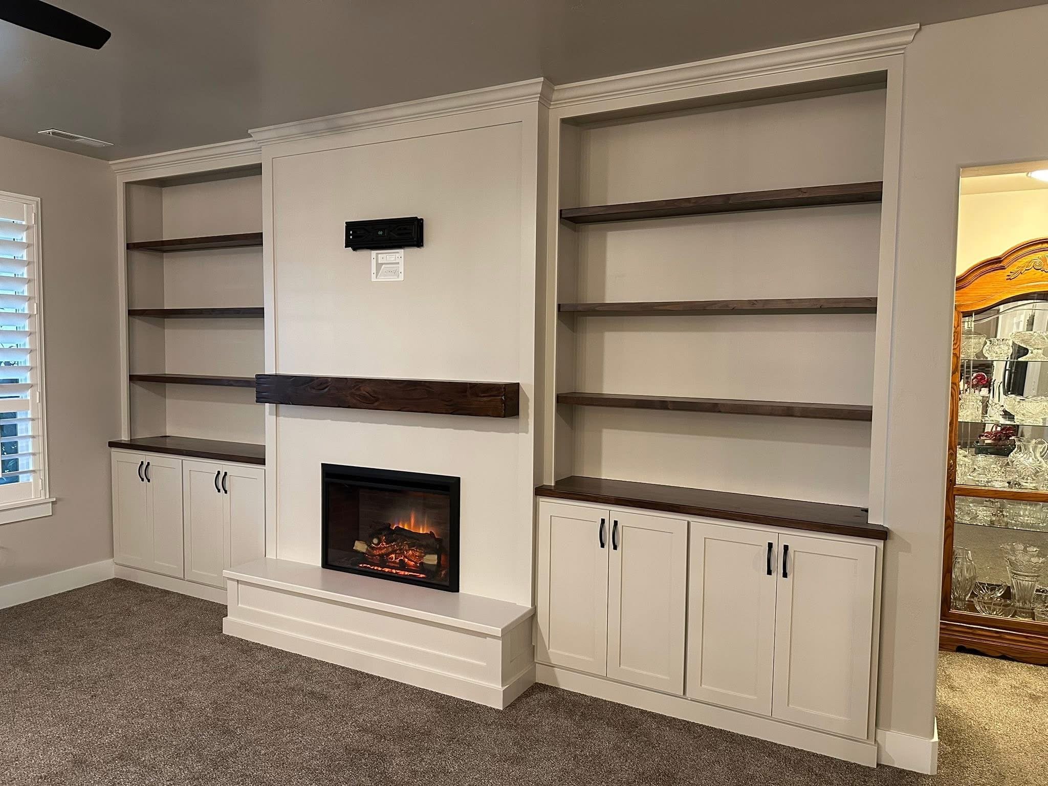 Modern built-in shelving with white cabinetry, dark stained wood shelves, and an electric fireplace feature wall in Meridian, Idaho.