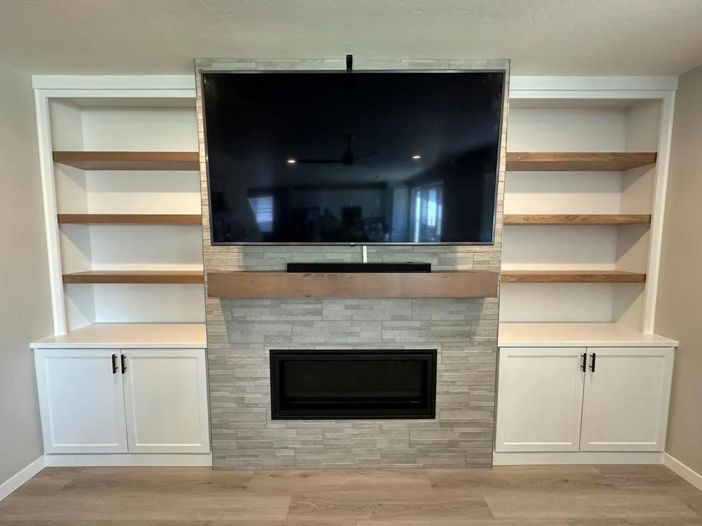 Custom fireplace entertainment wall with built-in storage cabinets, floating shelves, and a stone surround in Meridian, Idaho.