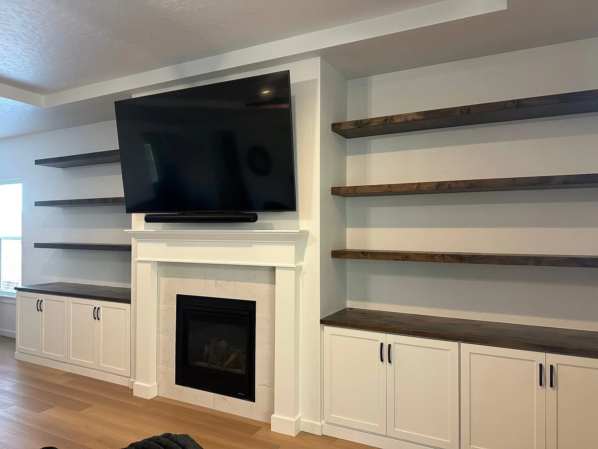 Custom floating wood shelves installed around a fireplace with white shaker cabinets in Star, Idaho.