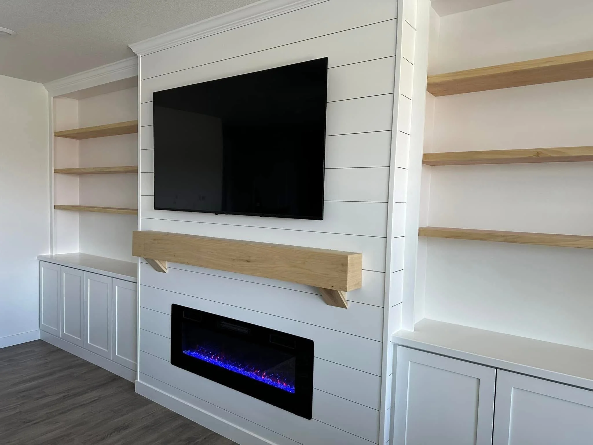 Custom electric fireplace feature wall with white shiplap, floating wood mantel, and built-in storage cabinets in Caldwell, Idaho.