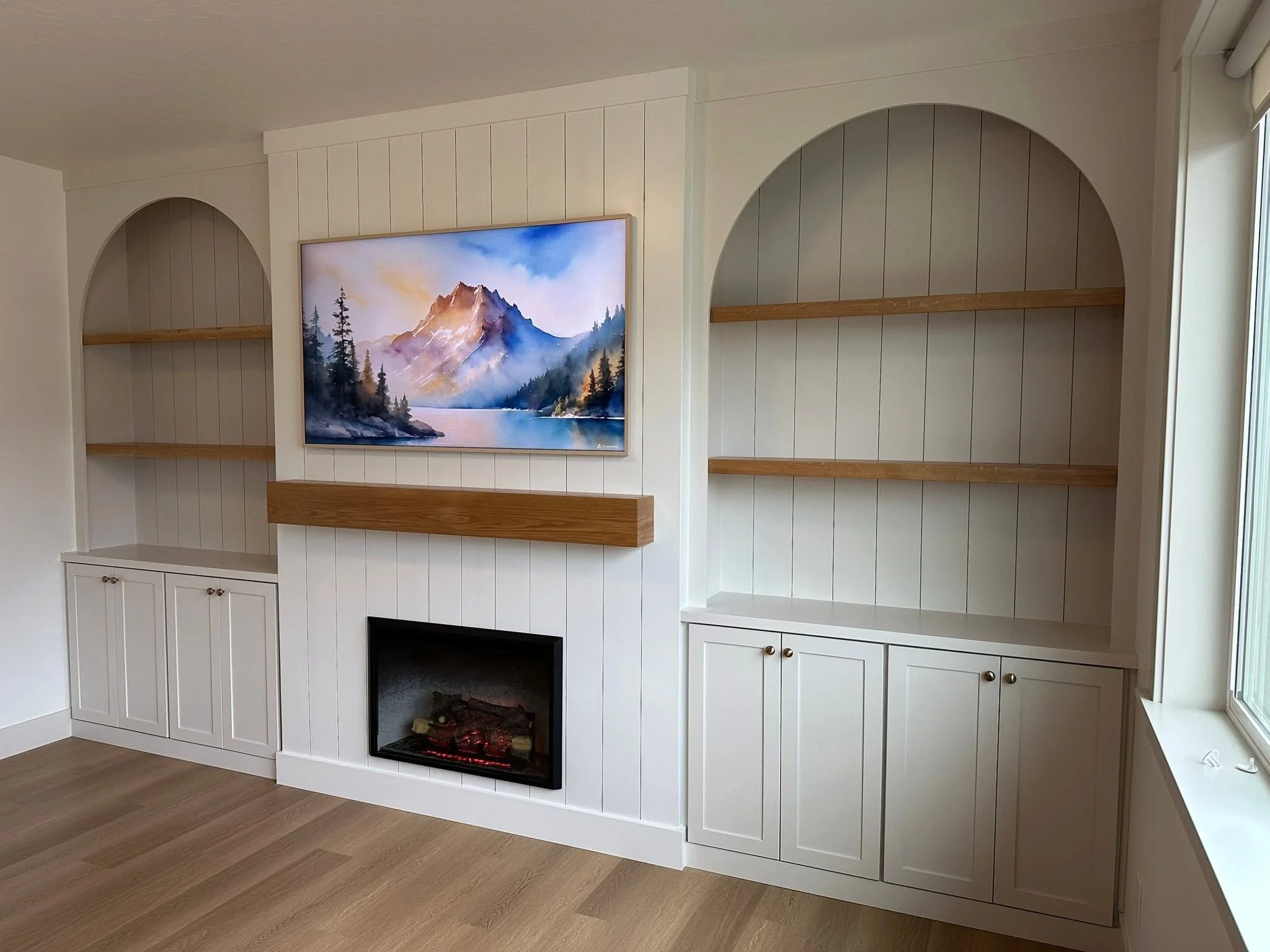Angled view of custom arched built-in shelving, a shiplap fireplace, and floating wood mantel in a Meridian, Idaho living room.