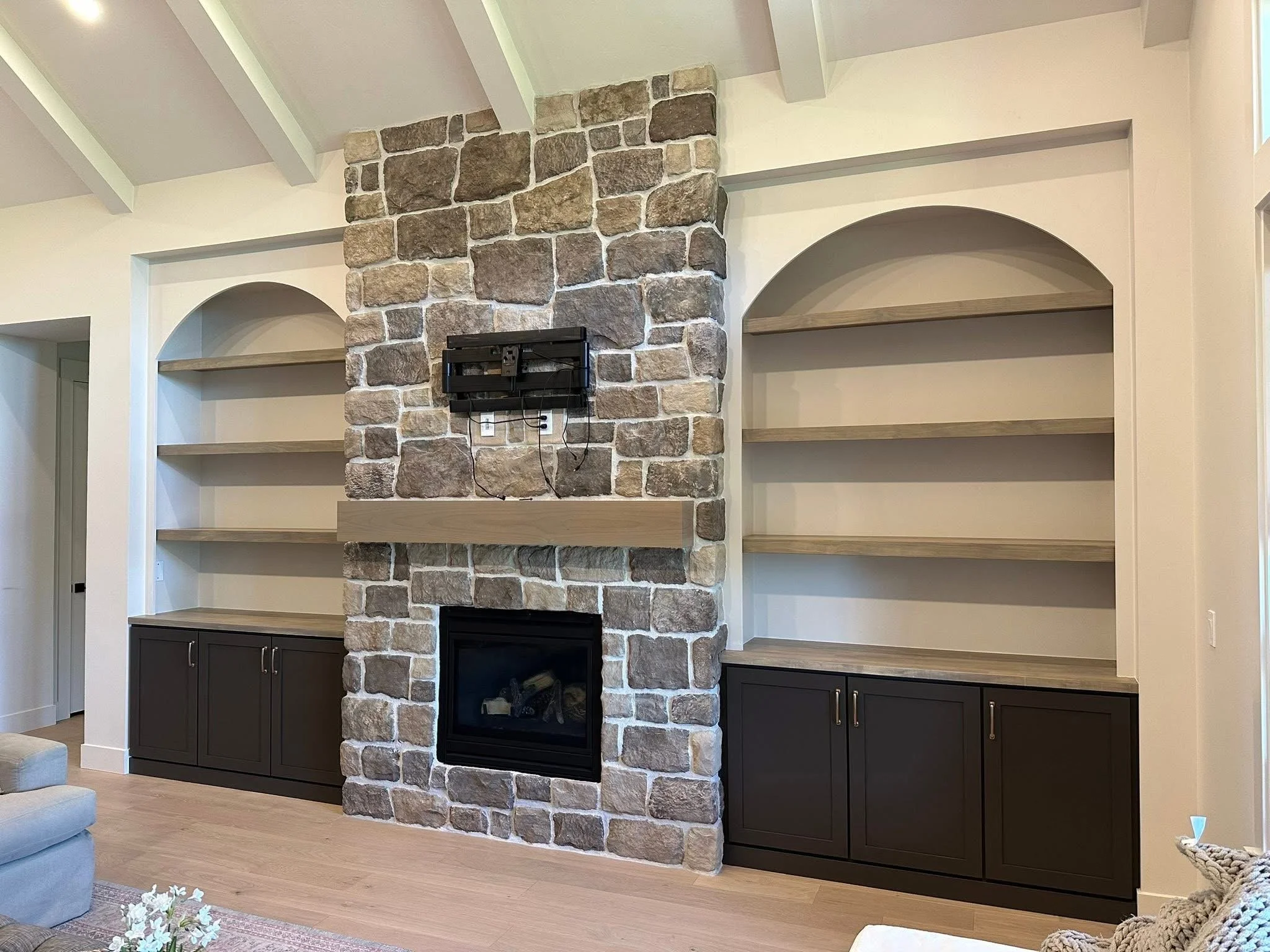 Floor-to-ceiling stone fireplace with custom arched built-in shelving and dark shaker cabinets in Kuna, Idaho.