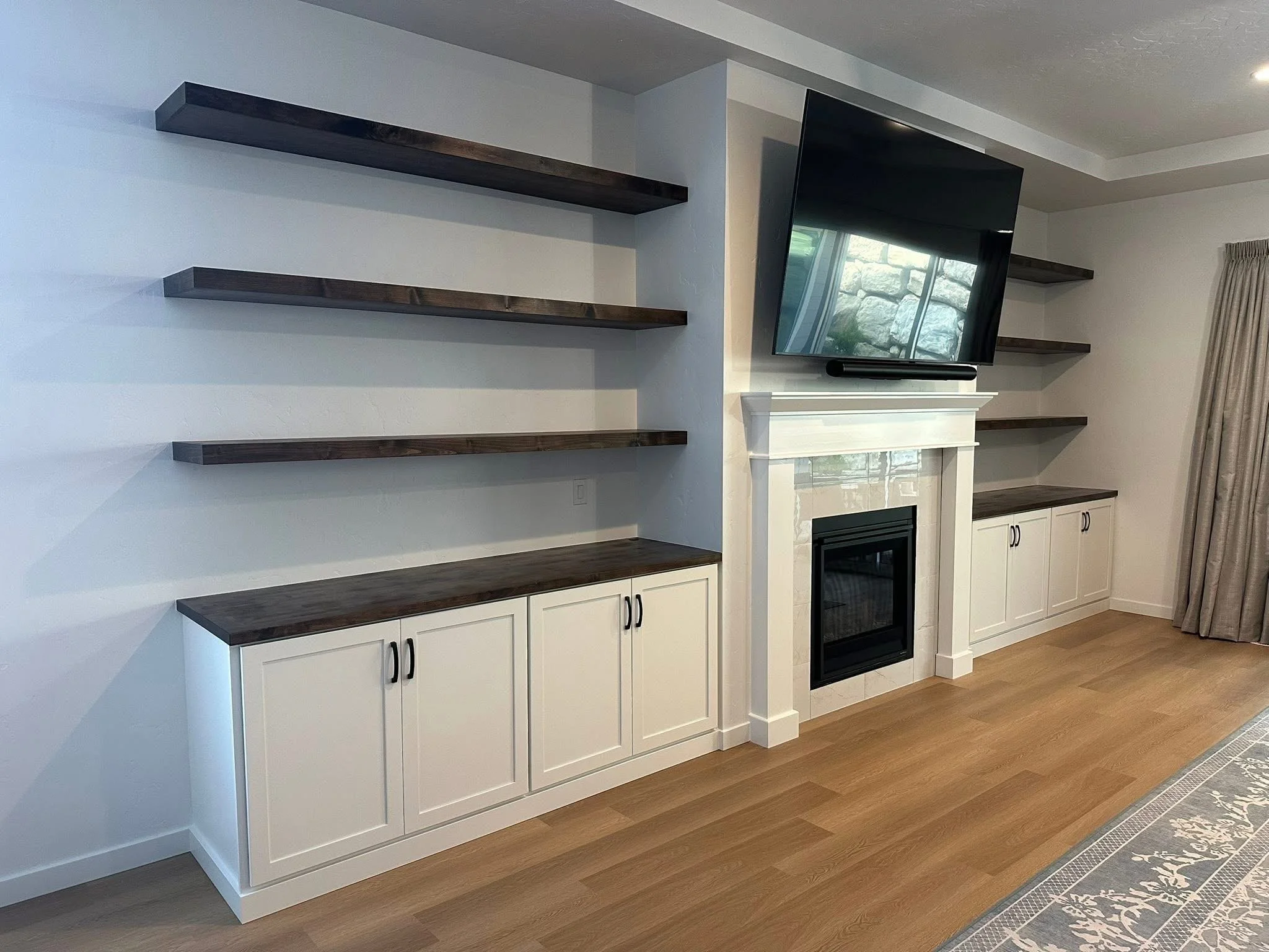 Modern built-in shelving with floating wood shelves and custom white shaker cabinets in a Star, Idaho living room.