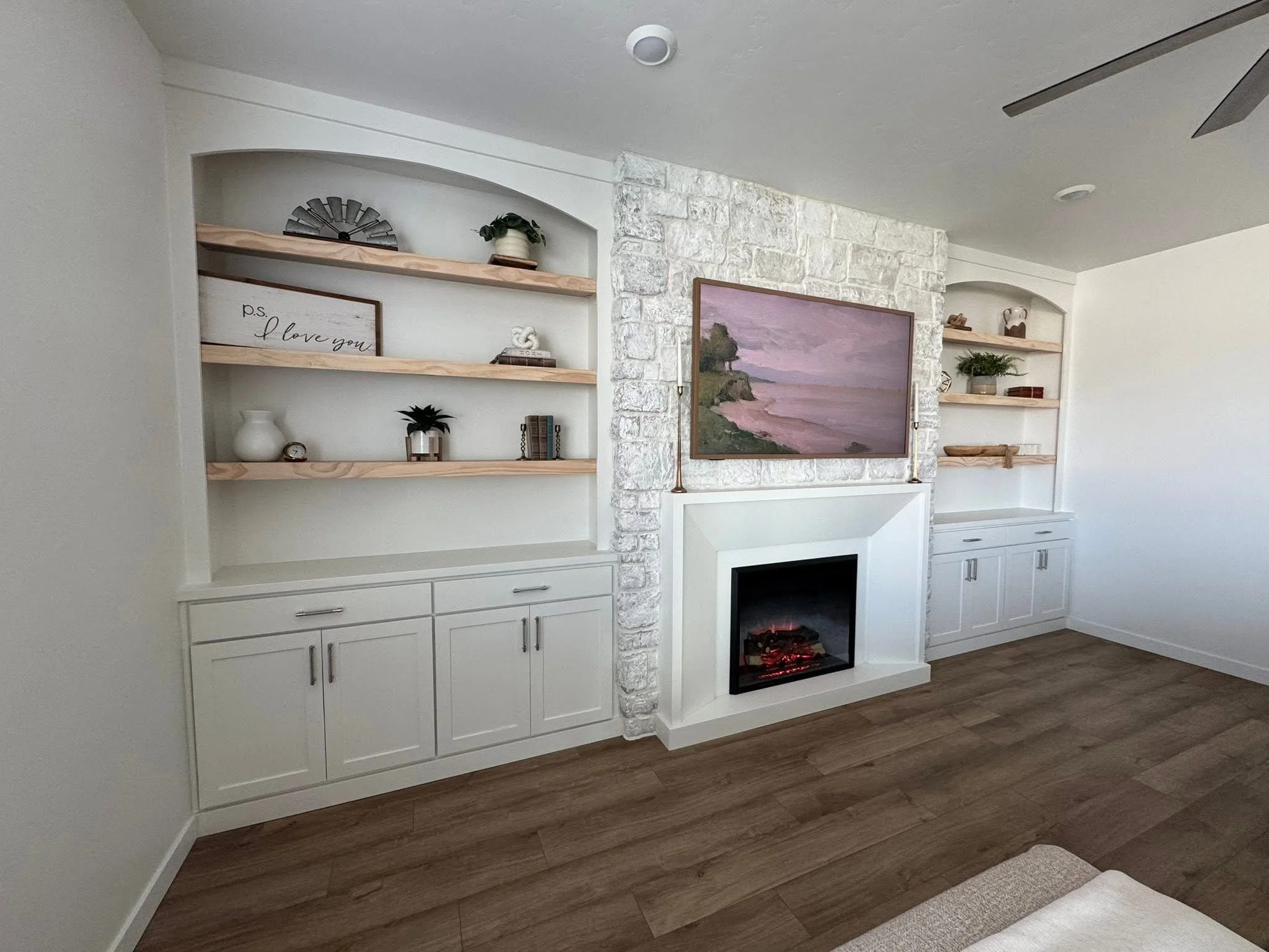 Angled view of a custom stone fireplace with arched built-in shelving and white shaker cabinets in Caldwell, Idaho.
