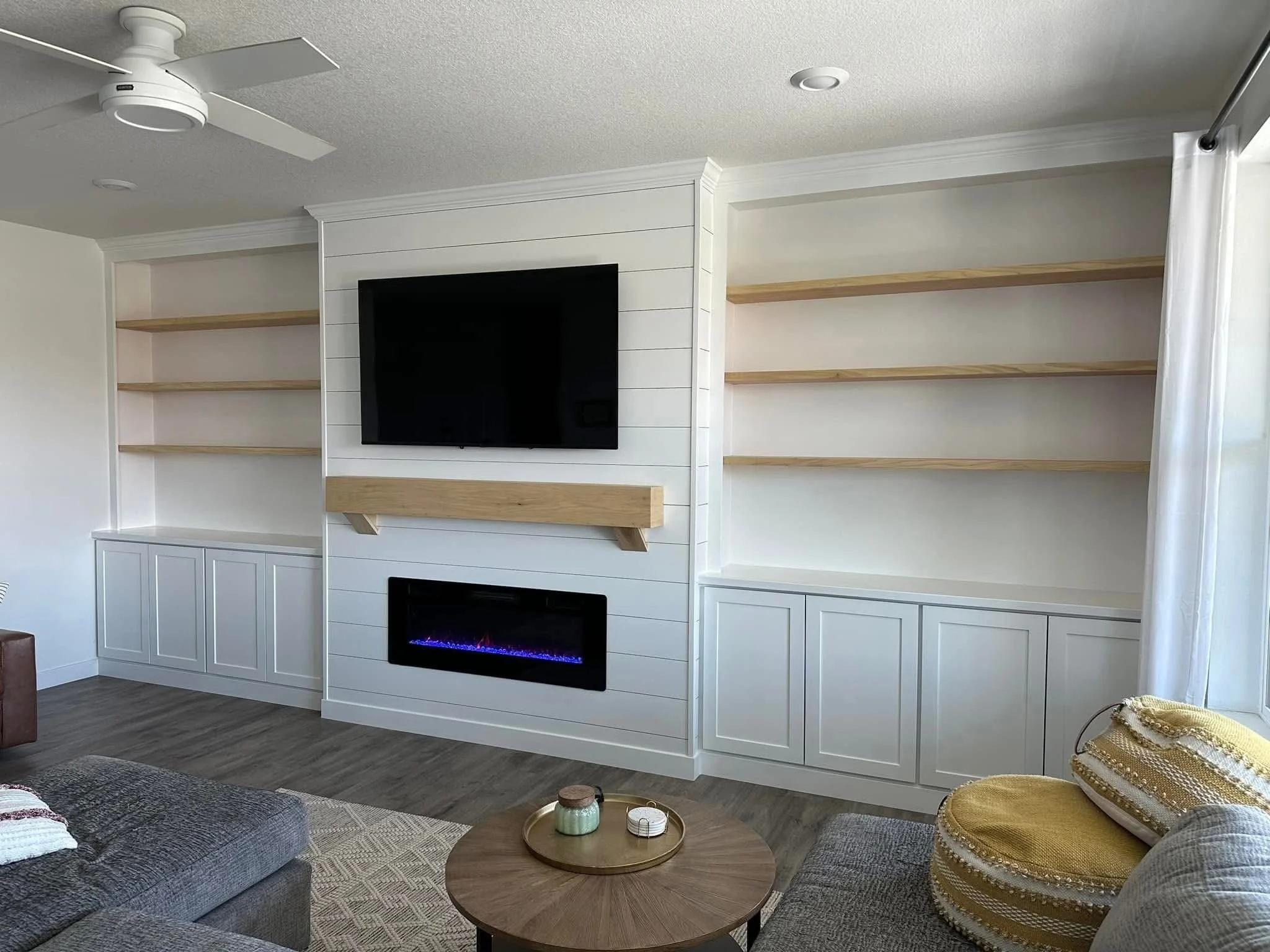 White built-in entertainment center with floating wood shelves, shiplap fireplace surround, and custom cabinetry in Caldwell, Idaho.