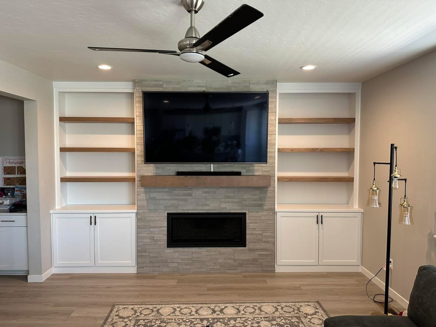 Custom entertainment center with built-in cabinets, floating wood shelves, and a stone fireplace in Meridian, Idaho.