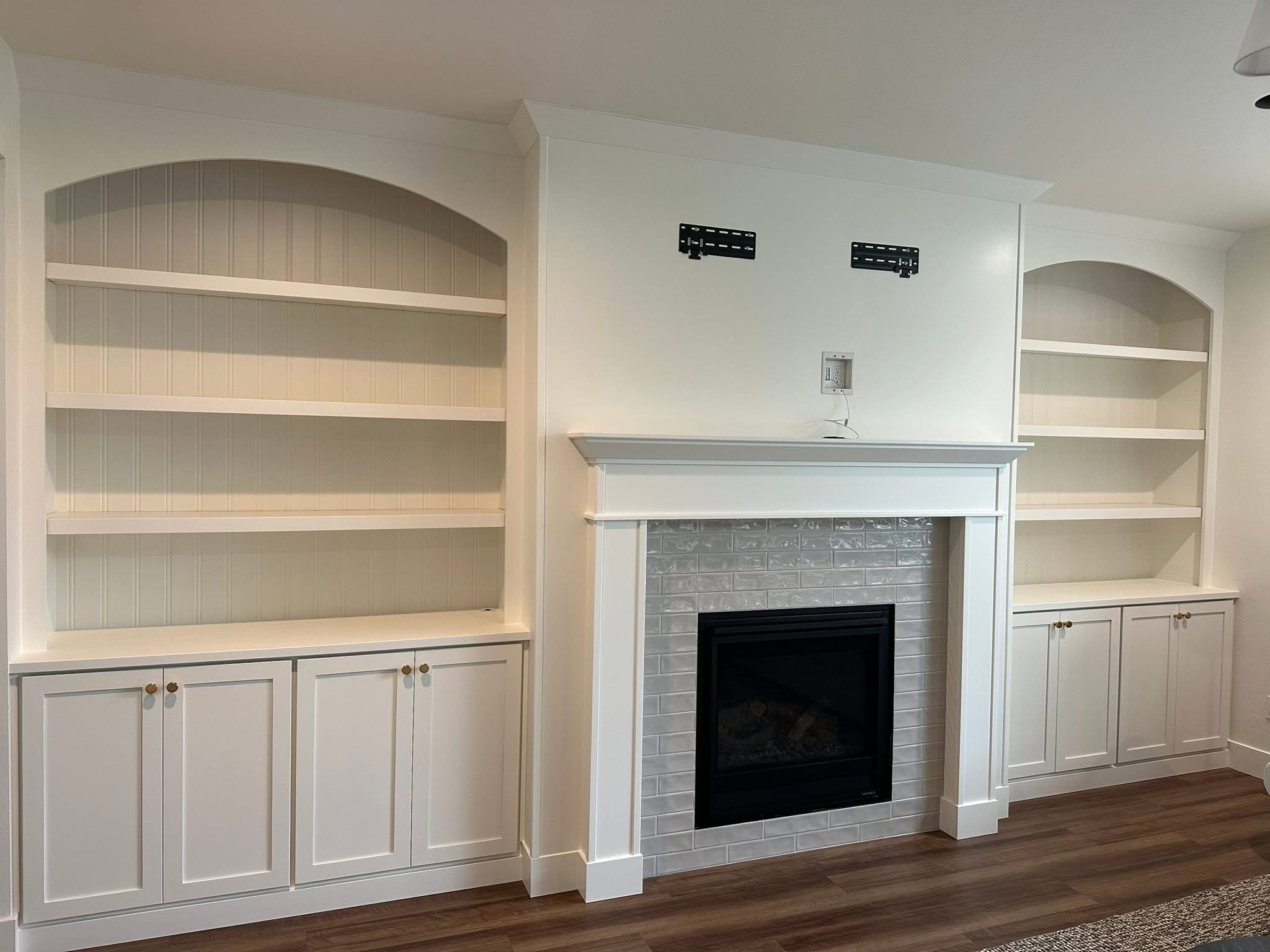 Custom white fireplace entertainment center with arched built-in shelving, beadboard backing, and shaker cabinets in Star, Idaho.