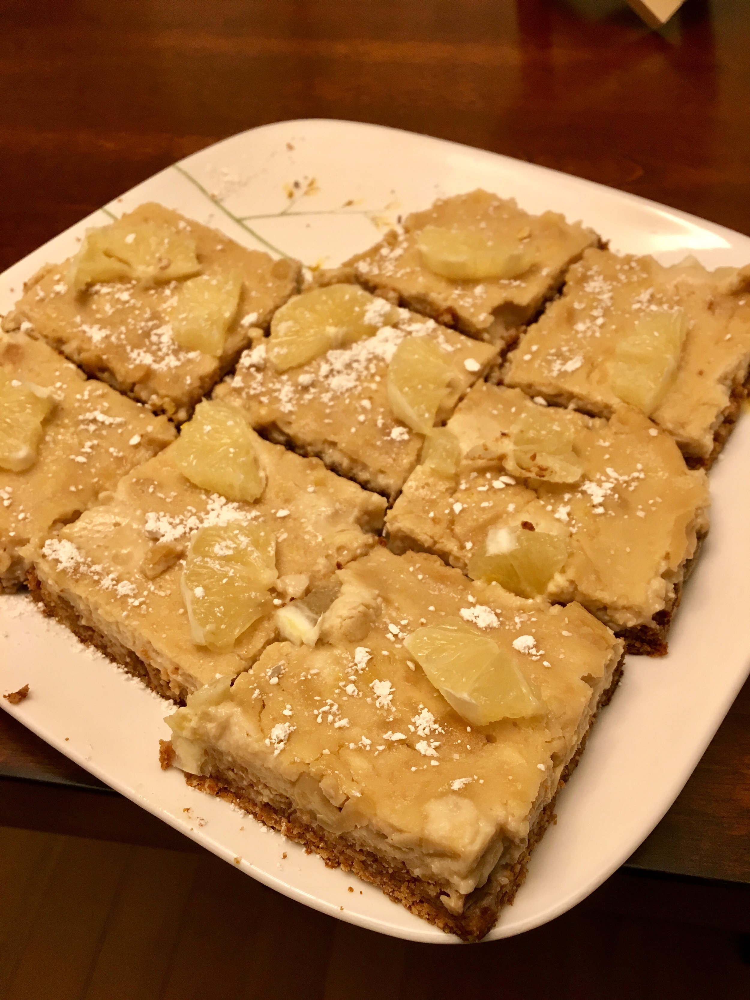 A plate with several square lemon bars topped with lemon slices and powdered sugar.