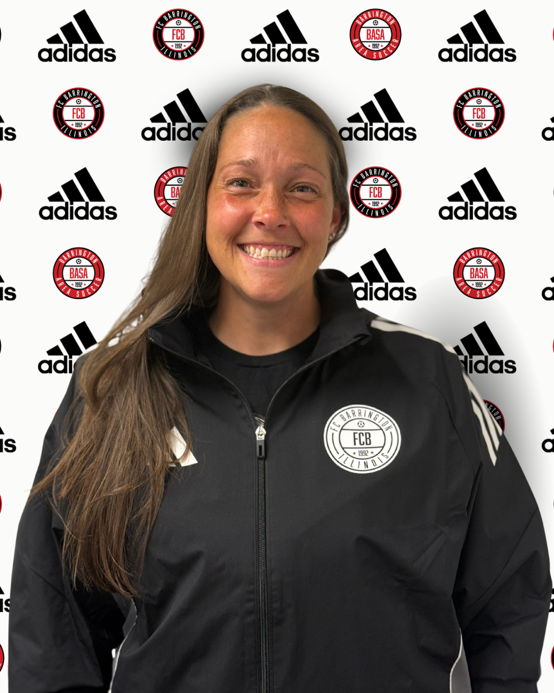 A smiling woman with long brown hair, wearing a gray Adidas jacket with a FCX logo, standing in front of a backdrop with repeating logos of Adidas and Barrington Area Soccer.