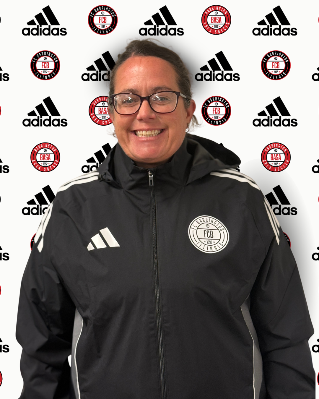 A woman smiling at a soccer event, standing in front of a backdrop with Adidas and FC Barrington Logos.