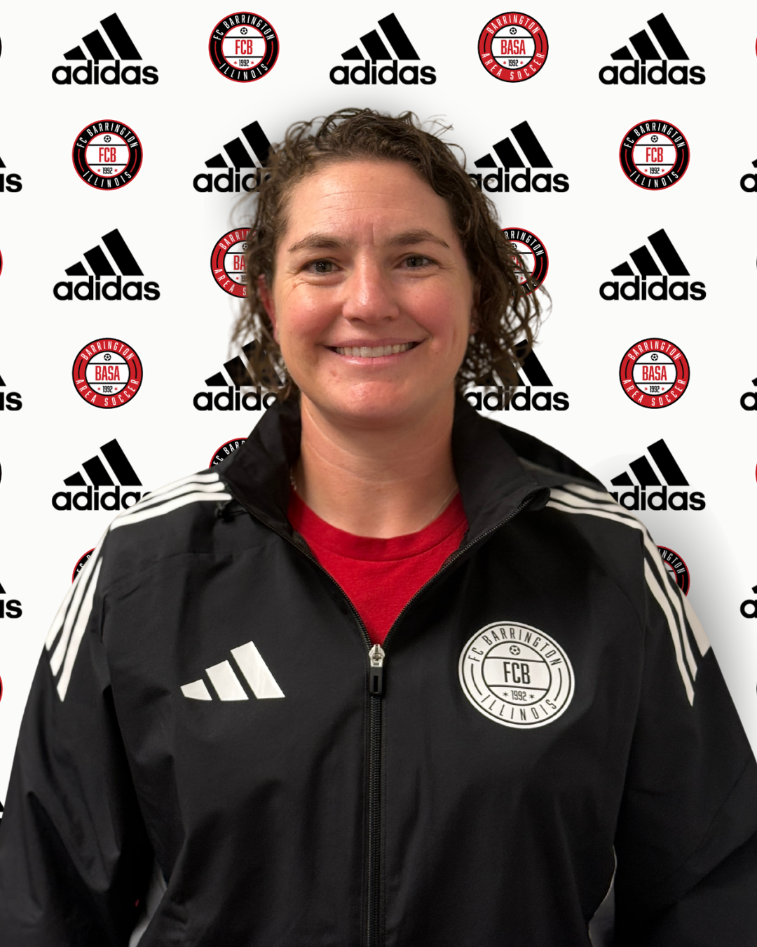 A smiling woman with curly brown hair wearing a navy blue FCX sweatshirt standing in front of a background with Adidas and Barrington FC logos.